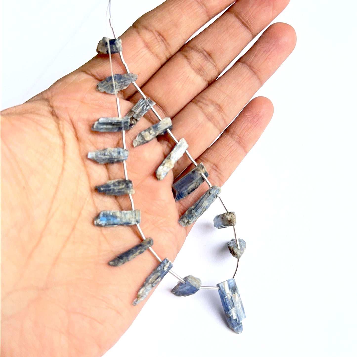 A person holds delicate strands of kyanite rough beads, showcasing their smooth design.