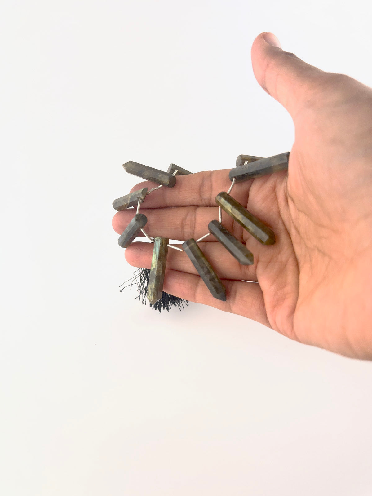 A person holds Labradorite pencil briolette beads, showing their faceted elongated design and colour play.