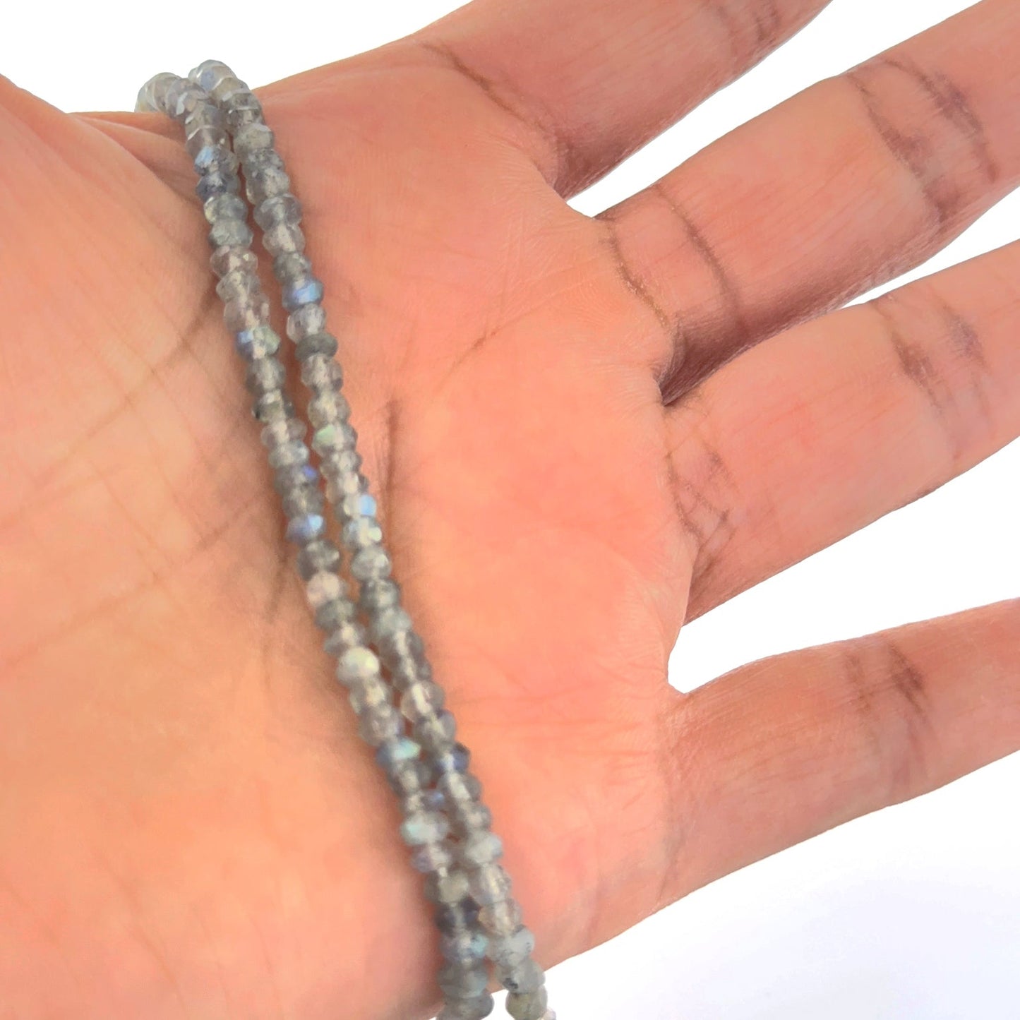 A person holds delicate strands of Labradorite beads, showcasing their faceted rondelle design