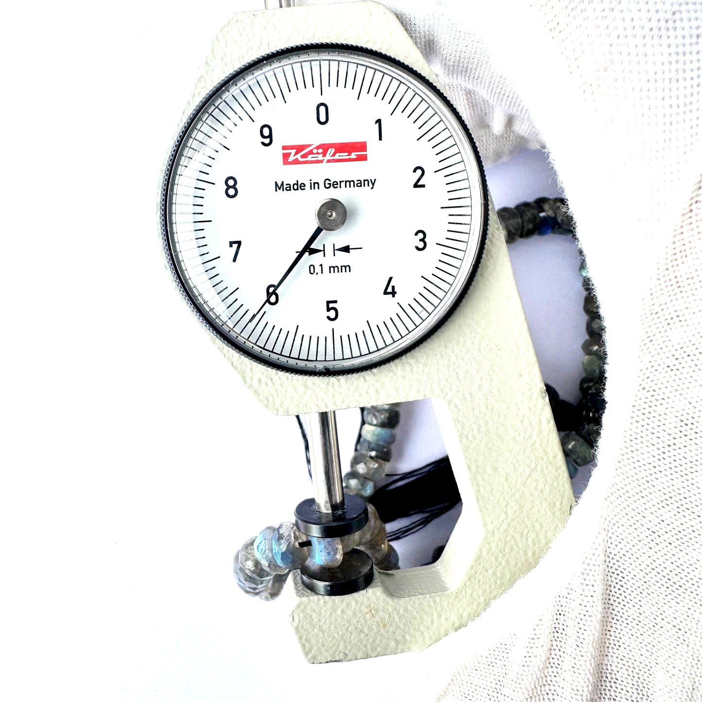 A dial gauge measures the Labradorite faceted rondelle 6.3-6.5mm gemstone.