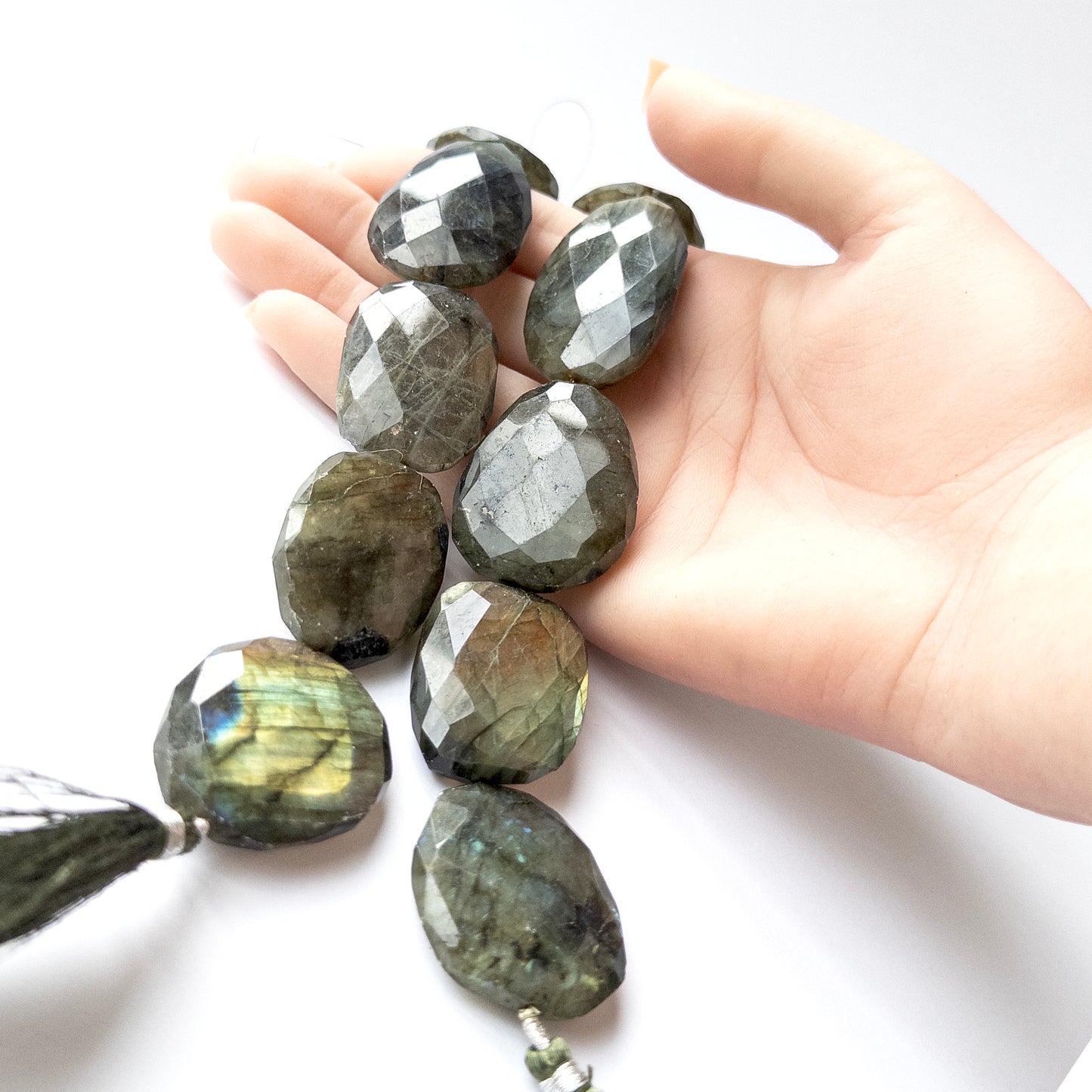 A person holds delicate pieces of Labradorite beads, showcasing their faceted oval design.