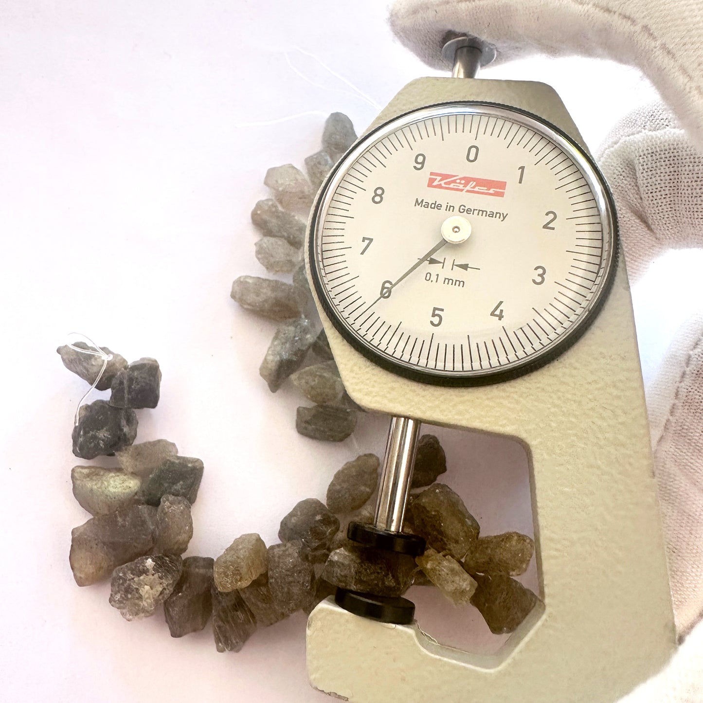 A dial gauge measures the labradorite rough side drilled 5.5–6mm gemstone.