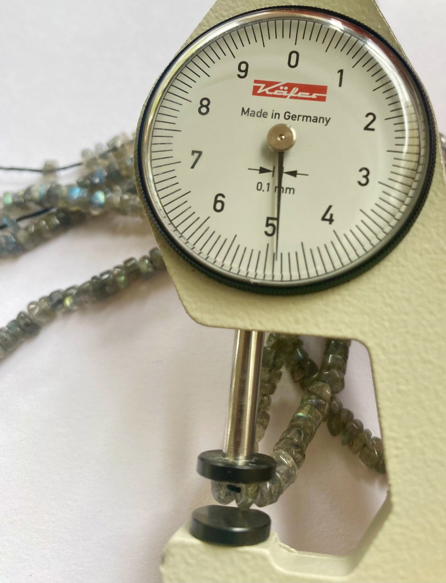 A dial gauge measures the Labradorite smooth wheel 4.5-5mm gemstone, ensuring precise sizing.