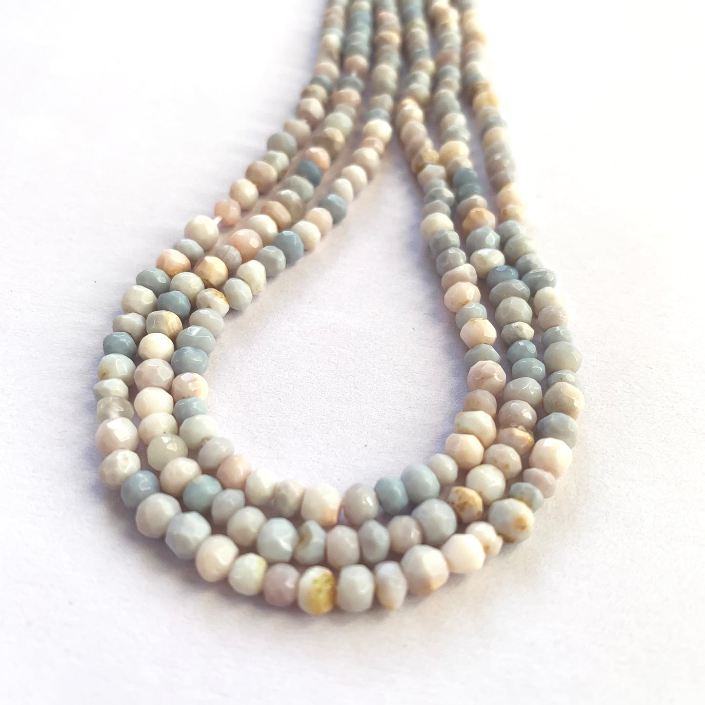 A person holds delicate strands of Lavender Opal beads, showcasing their smooth design.