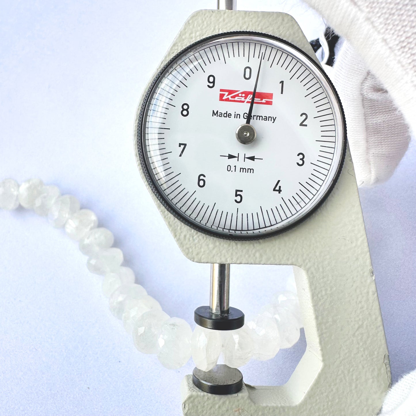 A dial gauge measures the moonstone faceted rondelle 10mm gemstone.