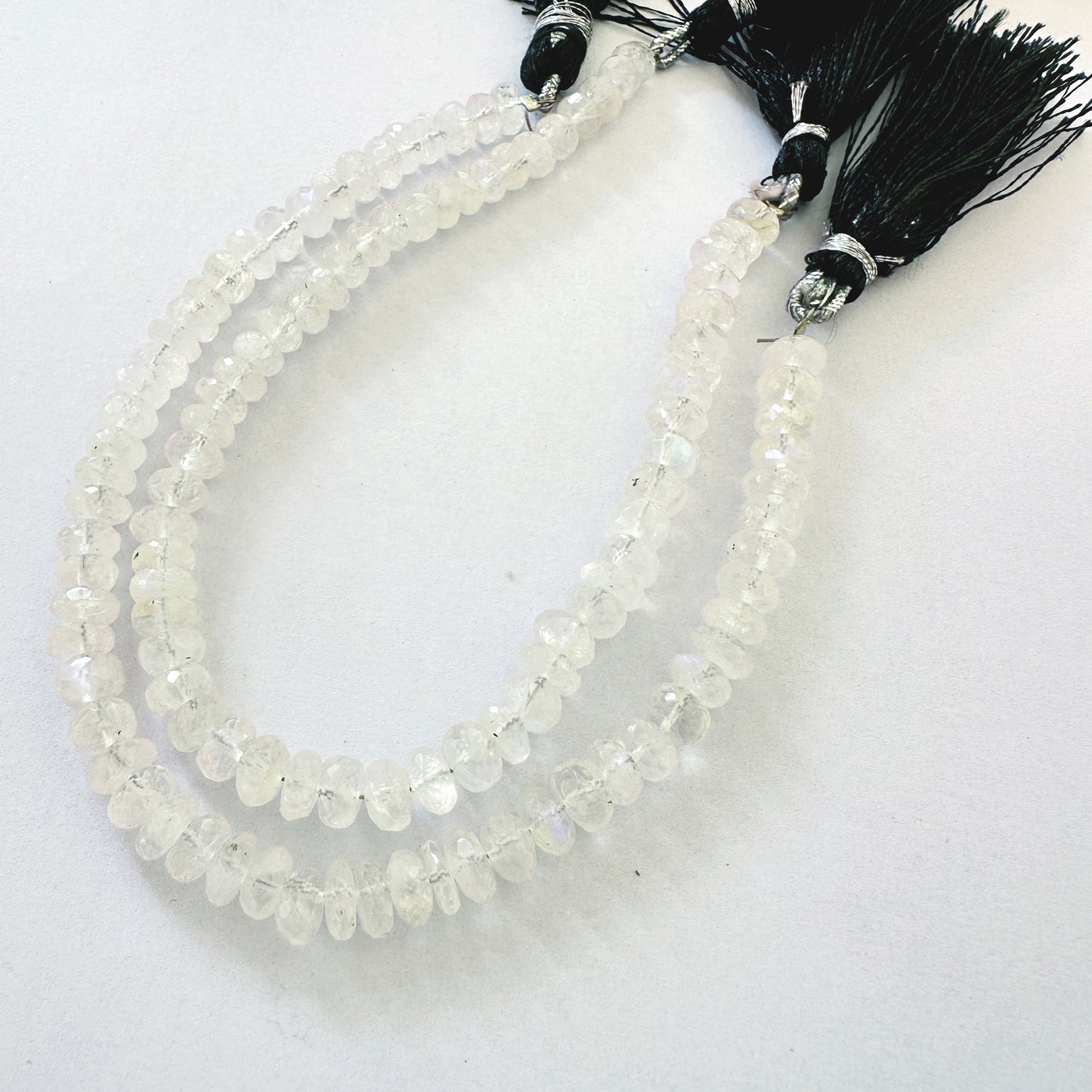 Smooth Moonstone rondelles with soft greys and creams displayed across beading thread.