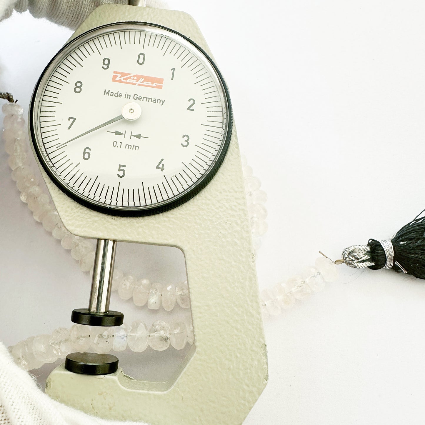 A dial gauge measures the Moonstone faceted rondelle 6.3–6.5mm gemstone.