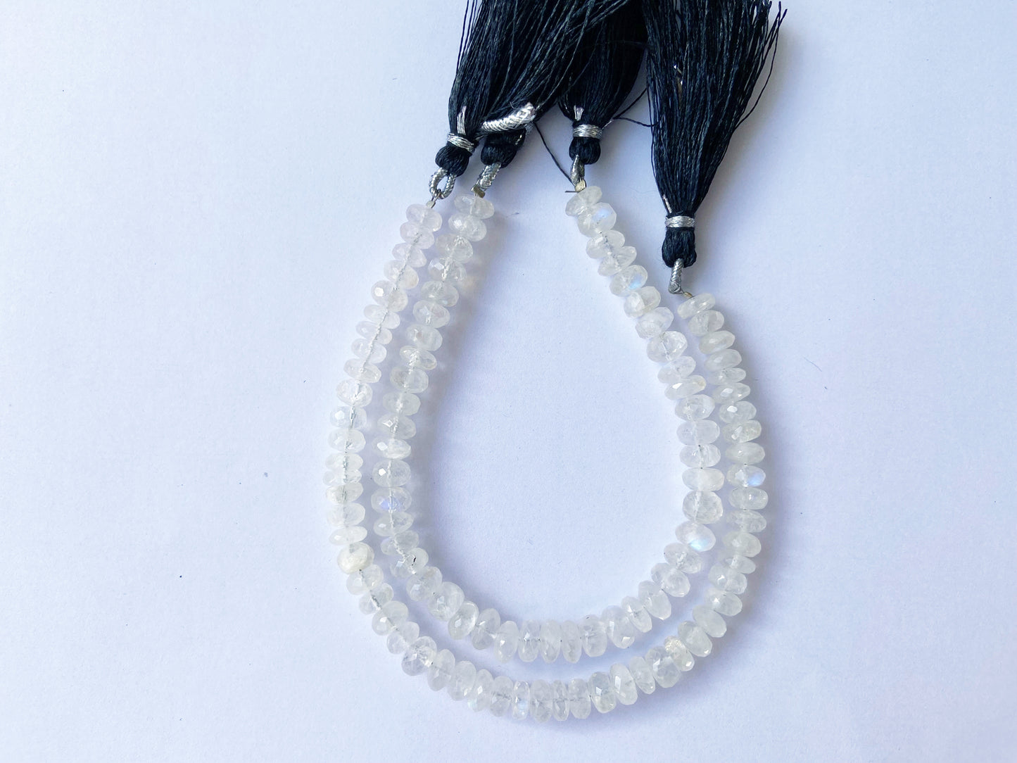 Glistening Moonstone beads with faceted surface aligned in uniform rows for jewellery crafting.