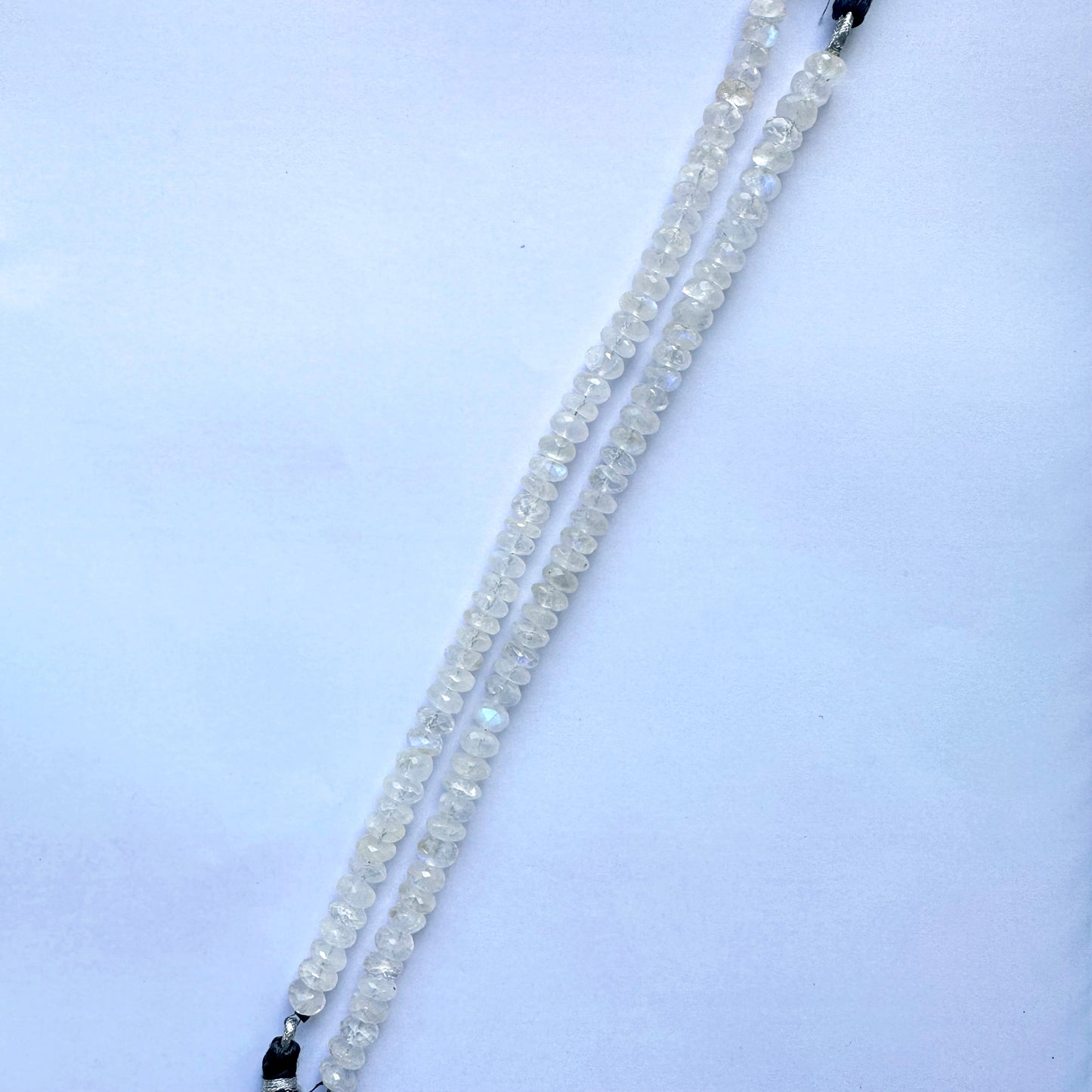 Hand-strung moonstone rondelle beads lined across a jewellery-making surface.
