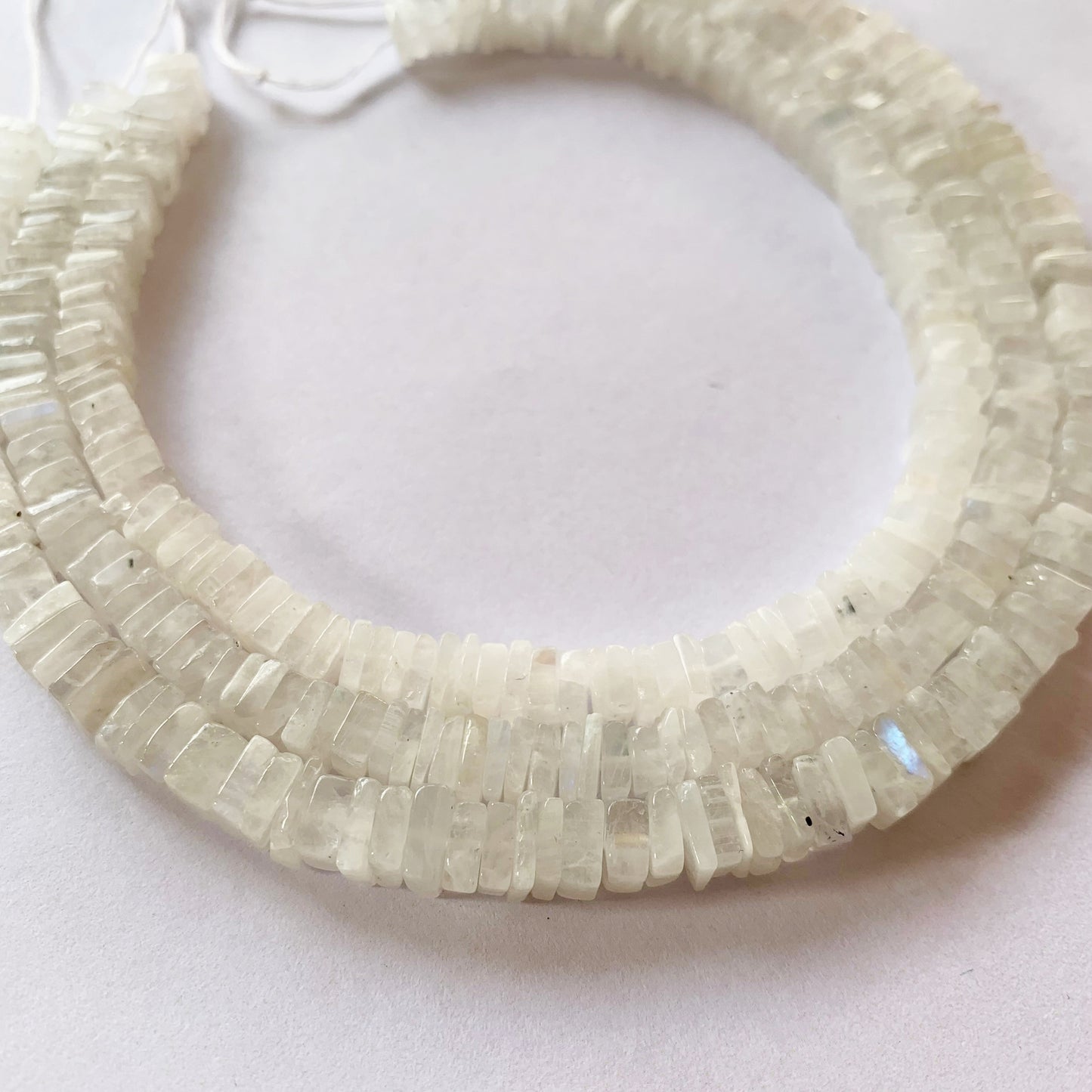 Moonstone heishi beads in square cut, reflecting light with subtle adularescence.