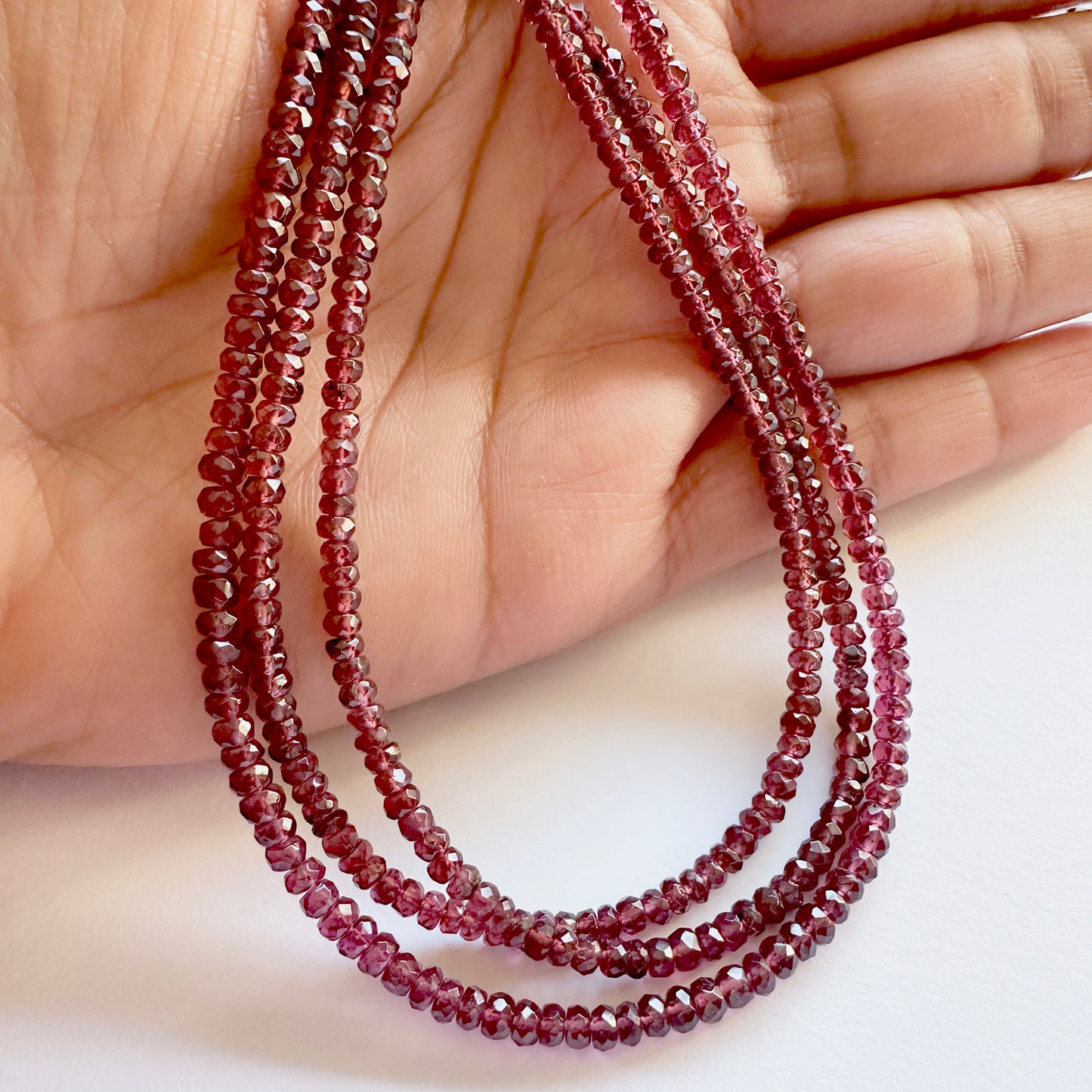 A person holds delicate strands of Mozambique Garnet beads, showcasing their faceted design.