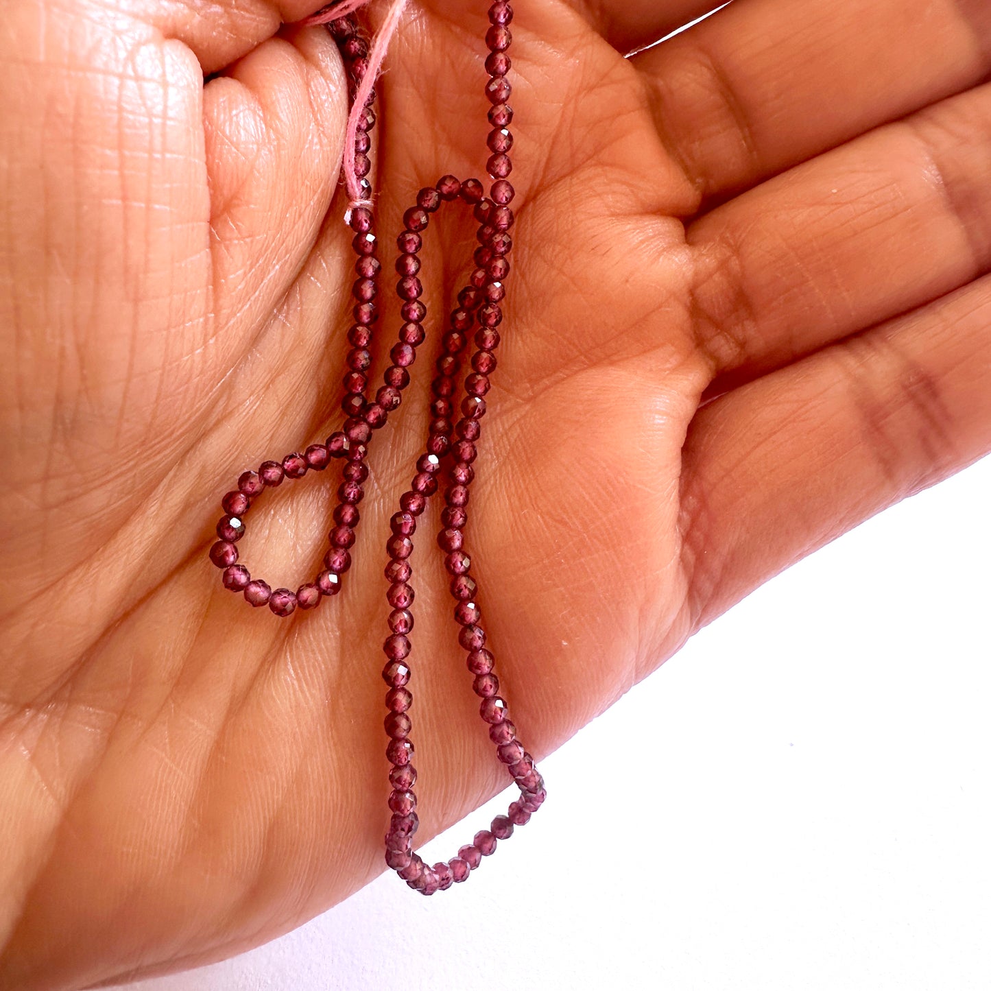 A person holds delicate strands of Mozambique Garnet beads, showcasing their smooth design.