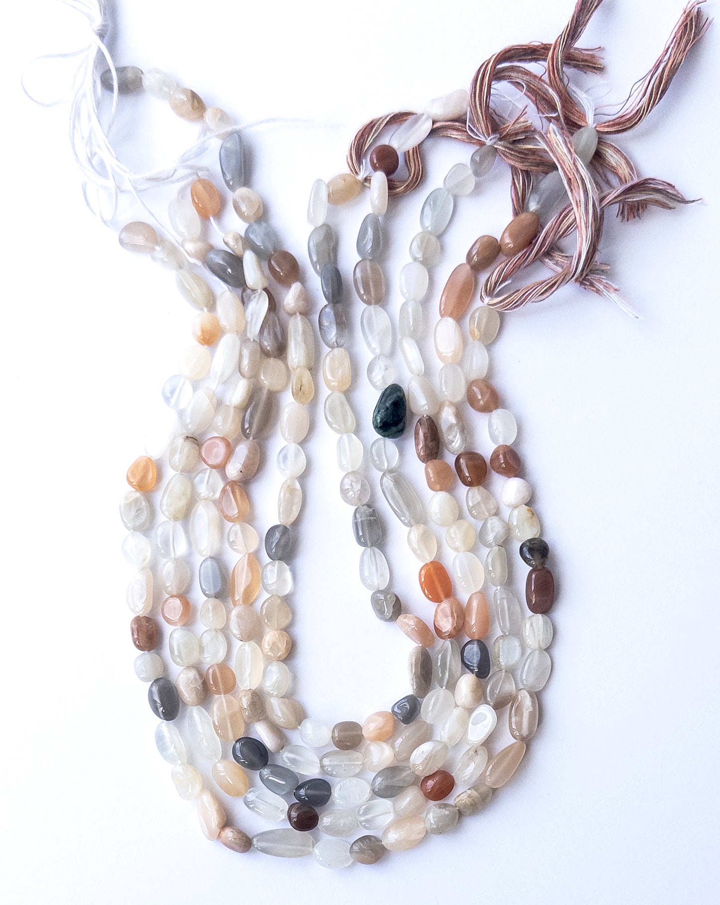 A person holds delicate strands of Multi Moonstone beads, showcasing their smooth tumble design.