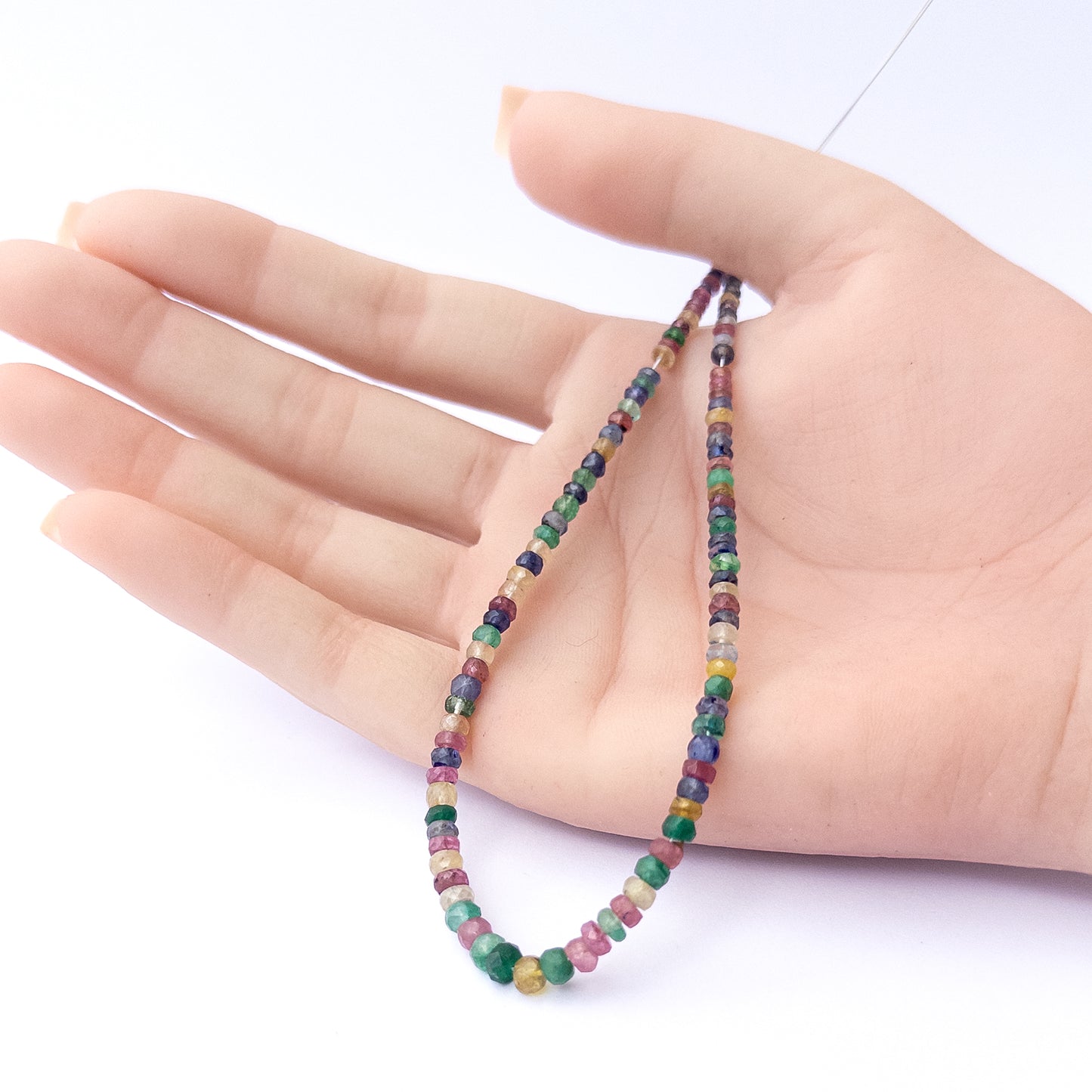 A person holds delicate strands of Multi Precious beads, showcasing their faceted rondelle design.