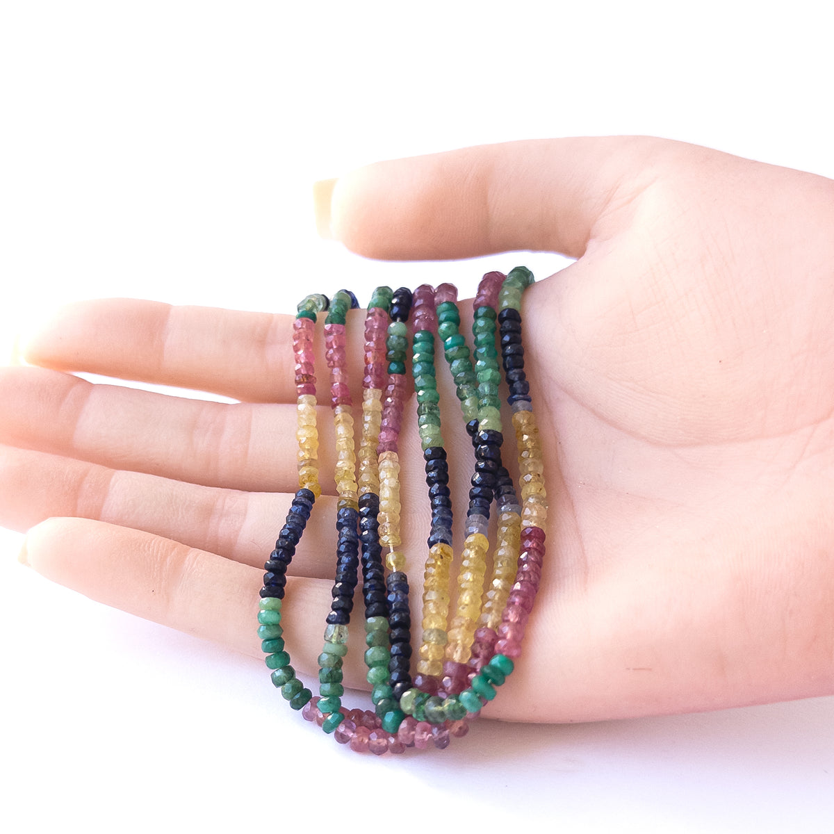 A person holds delicate strands of Multi Precious beads, showcasing their faceted rondelle design.