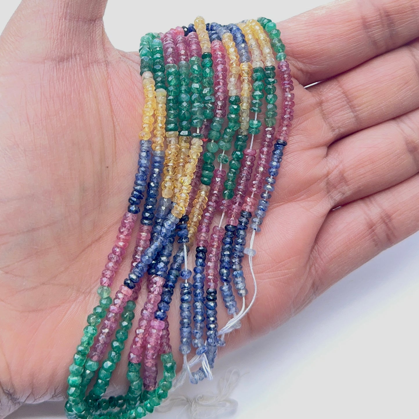 A person holds delicate strands of multi gemstone beads, showcasing their faceted design.
