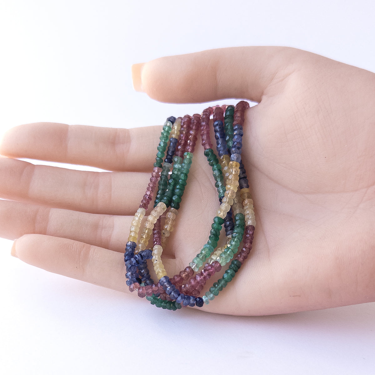 A person holds delicate strands of Multi Precious beads, showcasing their faceted rondelle design.