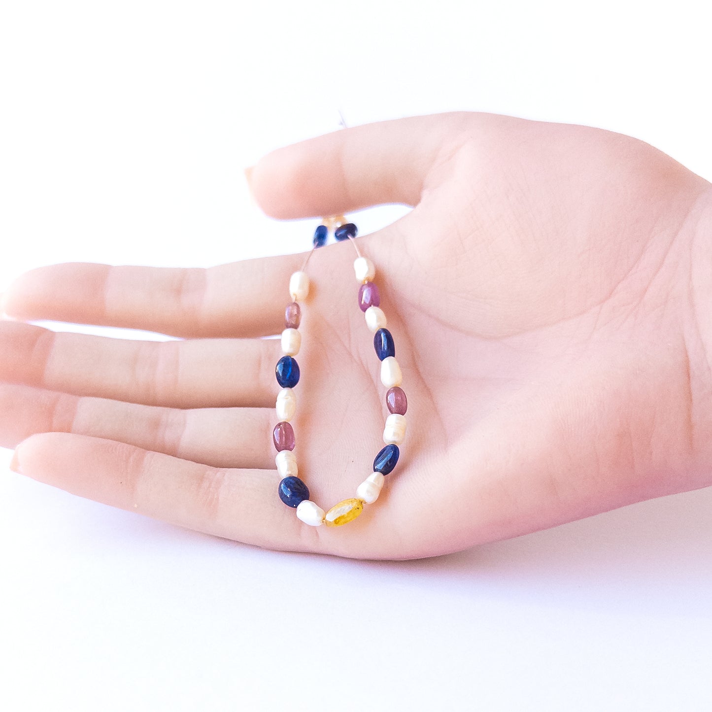 A person holds delicate strands of multi precious and freshwater pearl beads, showcasing their smooth oval design.