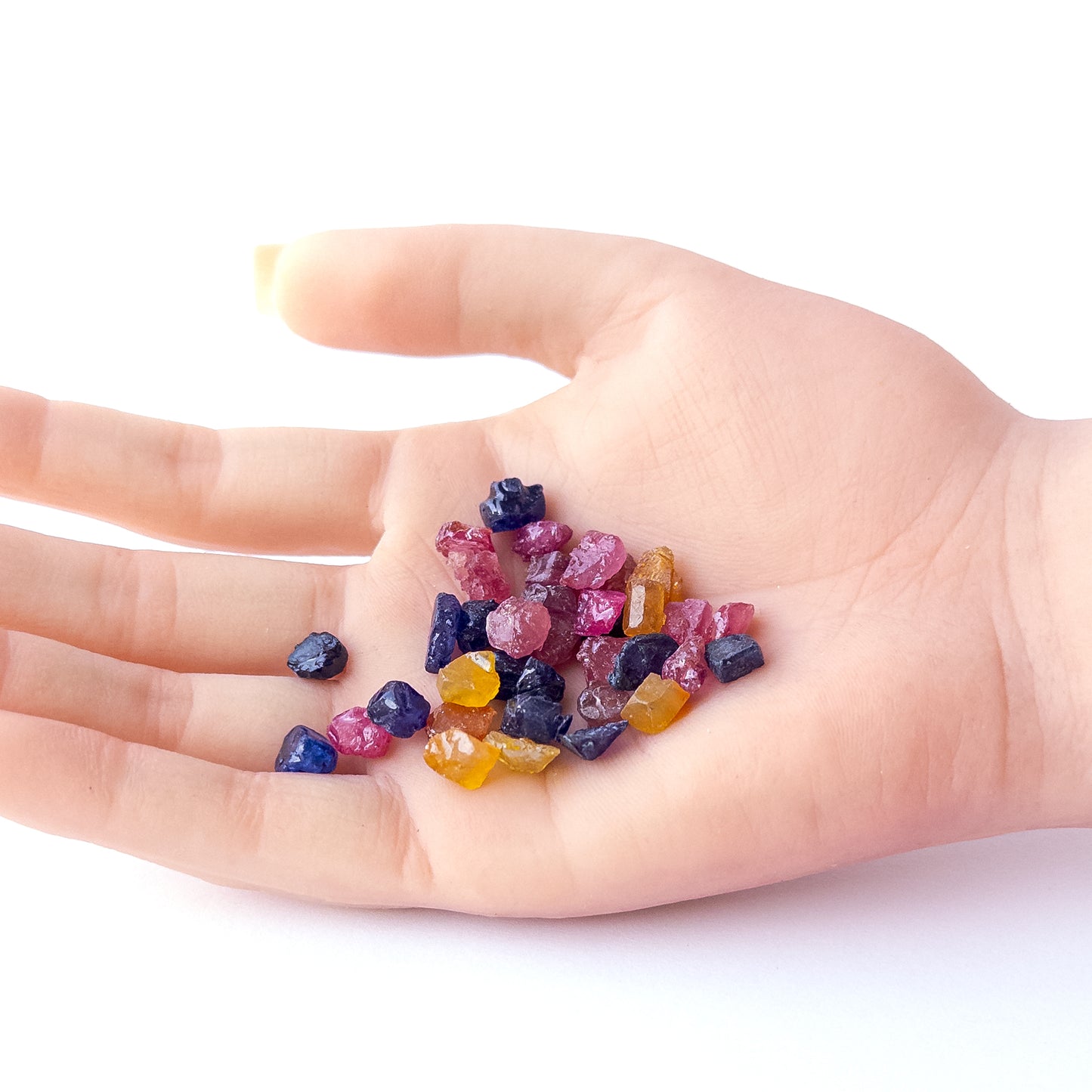 A person holds delicate pieces of Ruby, Blue Sapphire and Yellow Sapphire rough, showcasing their natural design.