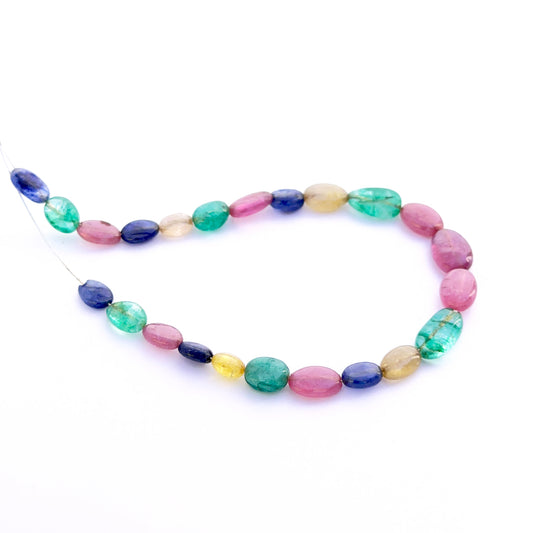 Close‑up of mixed ruby, blue sapphire and emerald smooth oval 6–7mm beads showing polished surfaces and vivid colour.