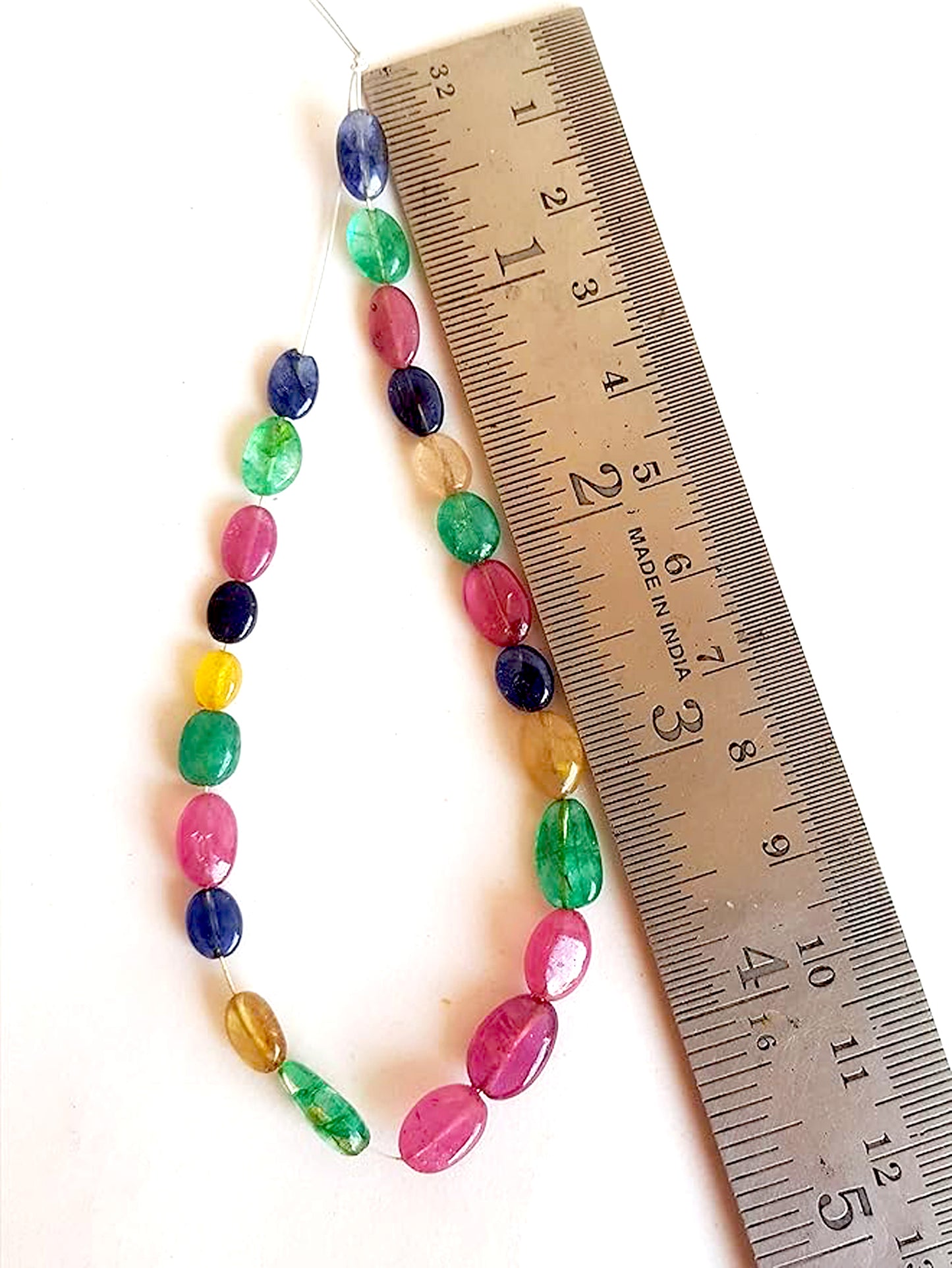 Multi stone oval beads next to a ruler in assorted colours laid out to enhance appeal and premium quality.