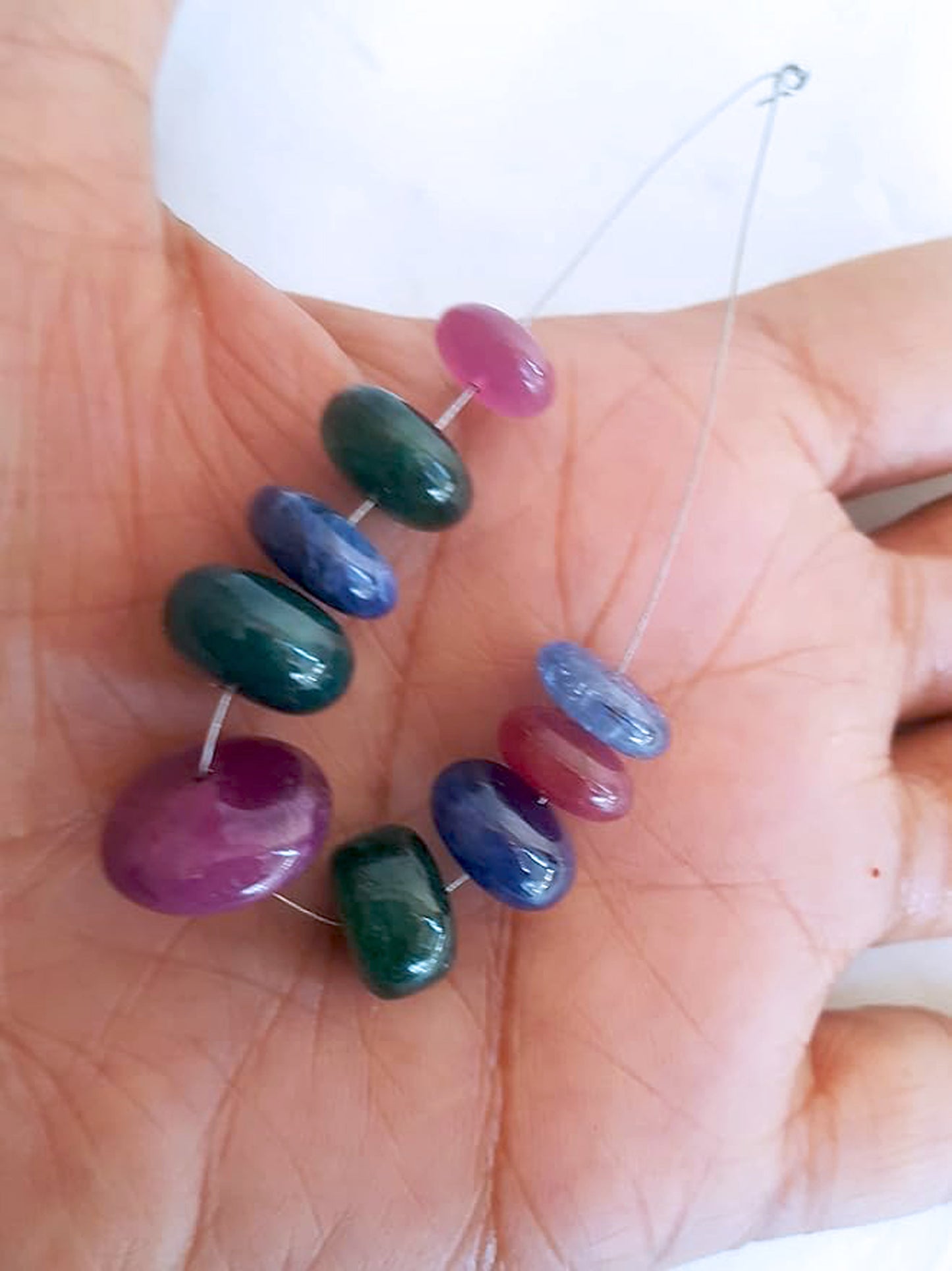 A person holds delicate strands of multi stone beads, showcasing their smooth design.