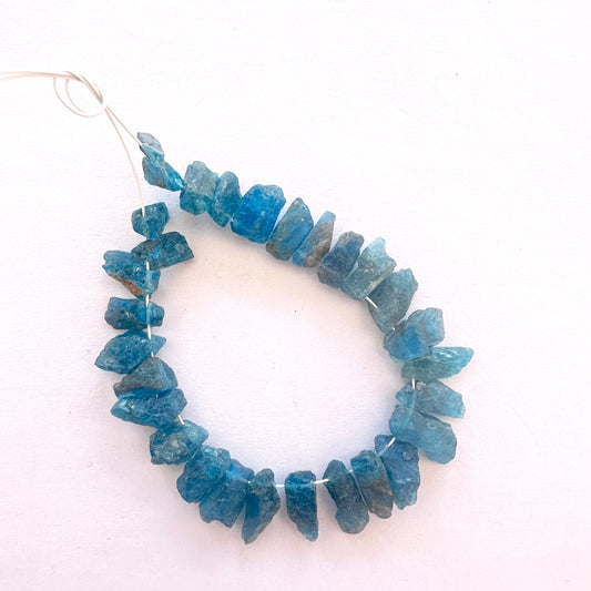 Close-up of raw Neon Apatite gemstones arranged in a 29-piece pack with natural texture.