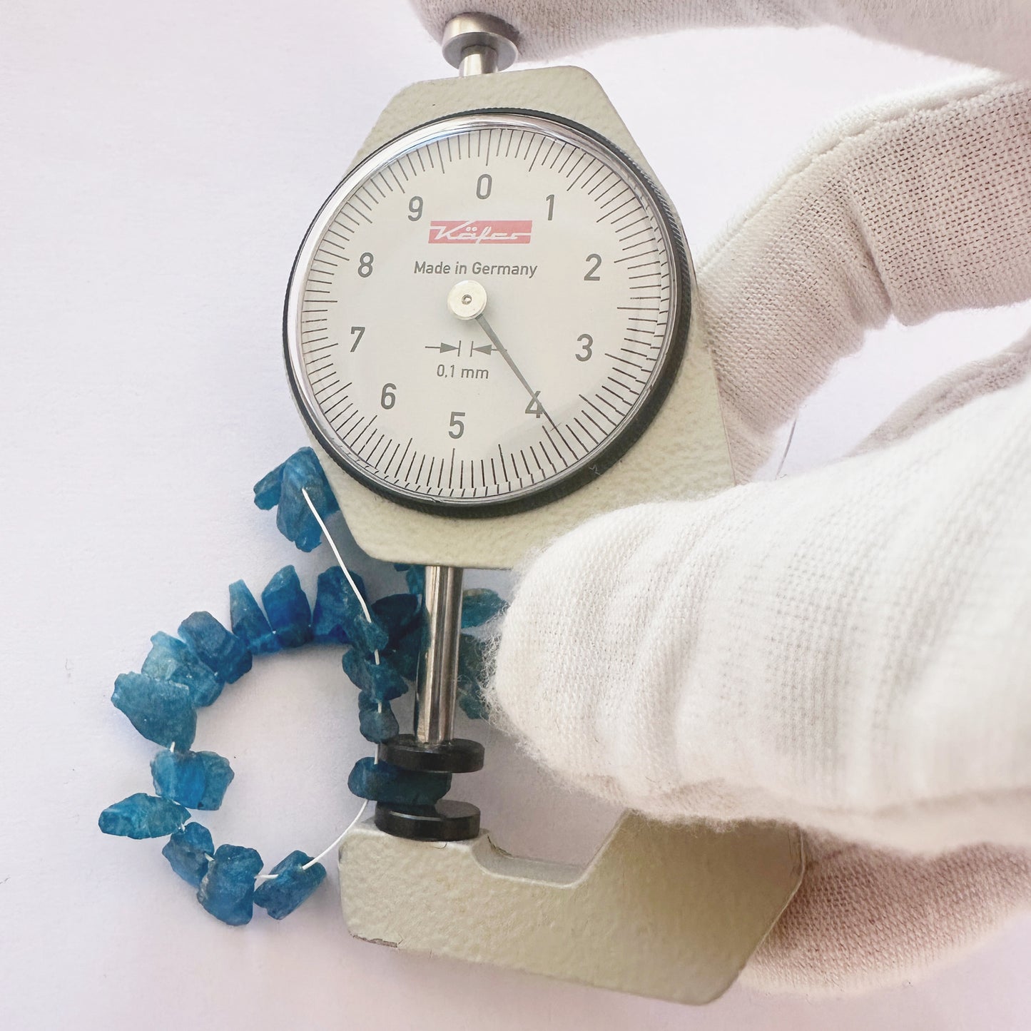 A dial gauge measures the Neon Apatite rough cut 4–5mm gemstone.