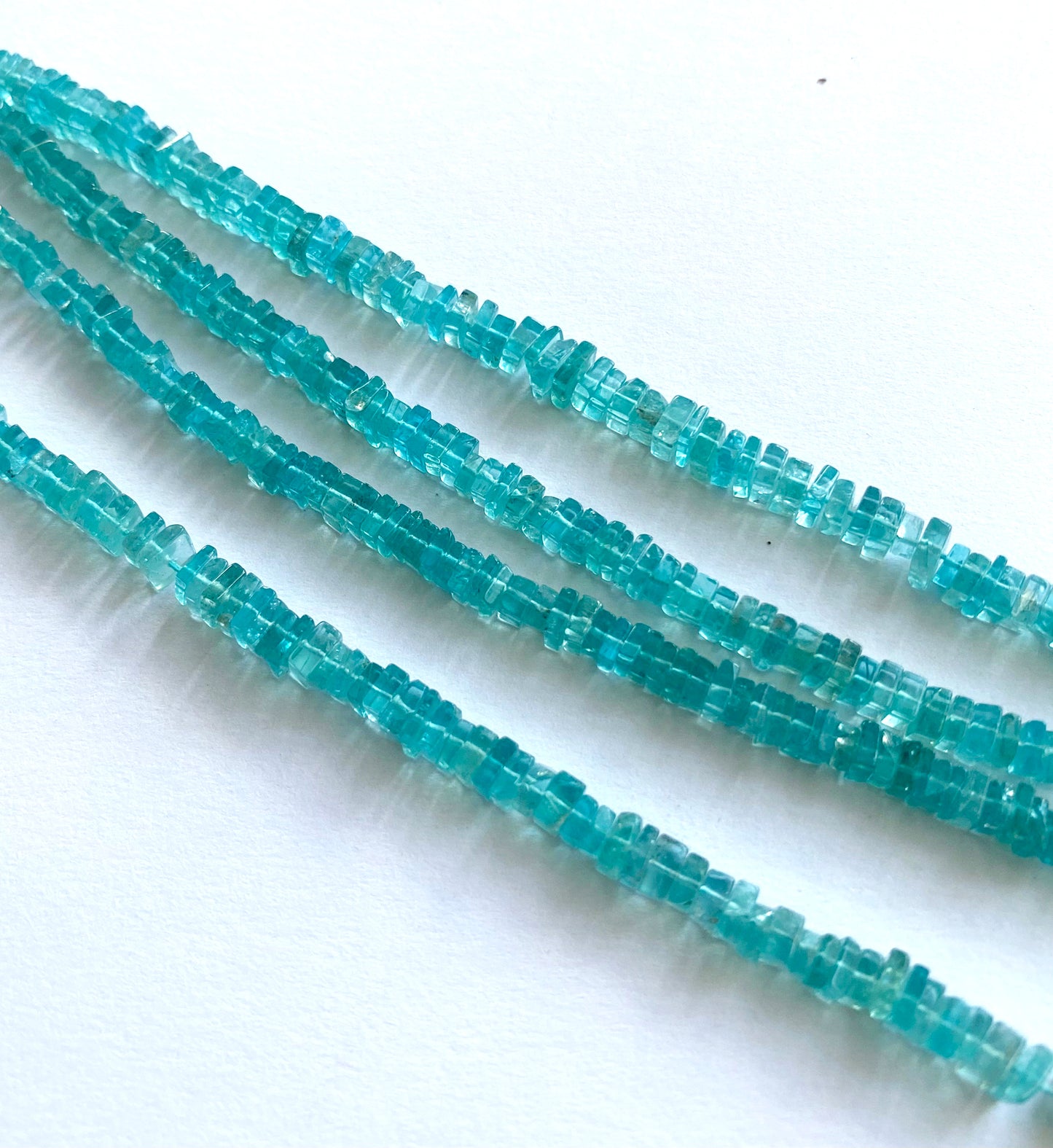 Close-up of smooth Neon Apatite square beads showing their 4.5–5.5mm size and polished finish.