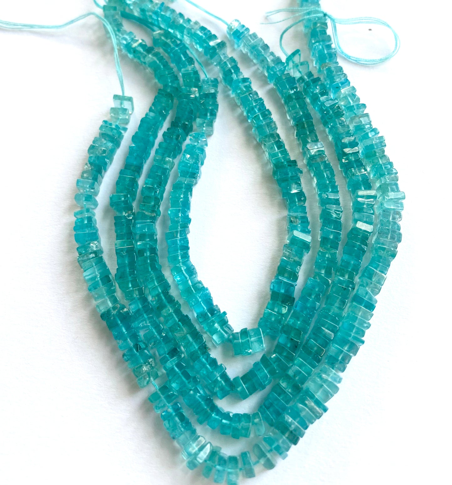 Neon Apatite heishi beads arranged in a neat strand, reflecting light with a luminous glow.