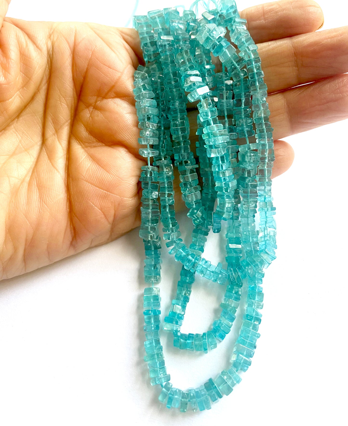 A person holds delicate strands of Neon Apatite beads, showcasing their smooth design.