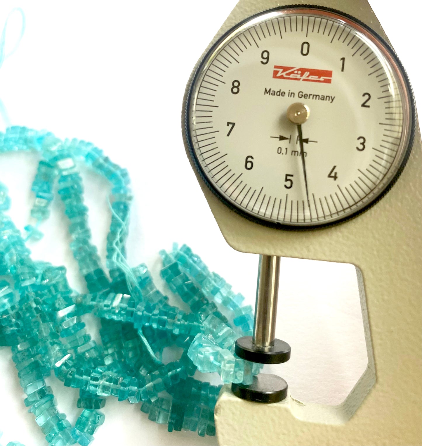 A dial gauge measures the Neon Apatite smooth square heishi 4.5–5.5mm gemstone.