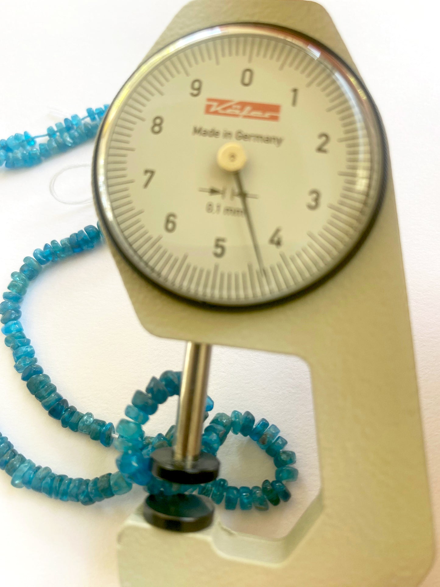 A dial gauge measures the neon apatite smooth wheel 3.5mm to 4mm gemstone.