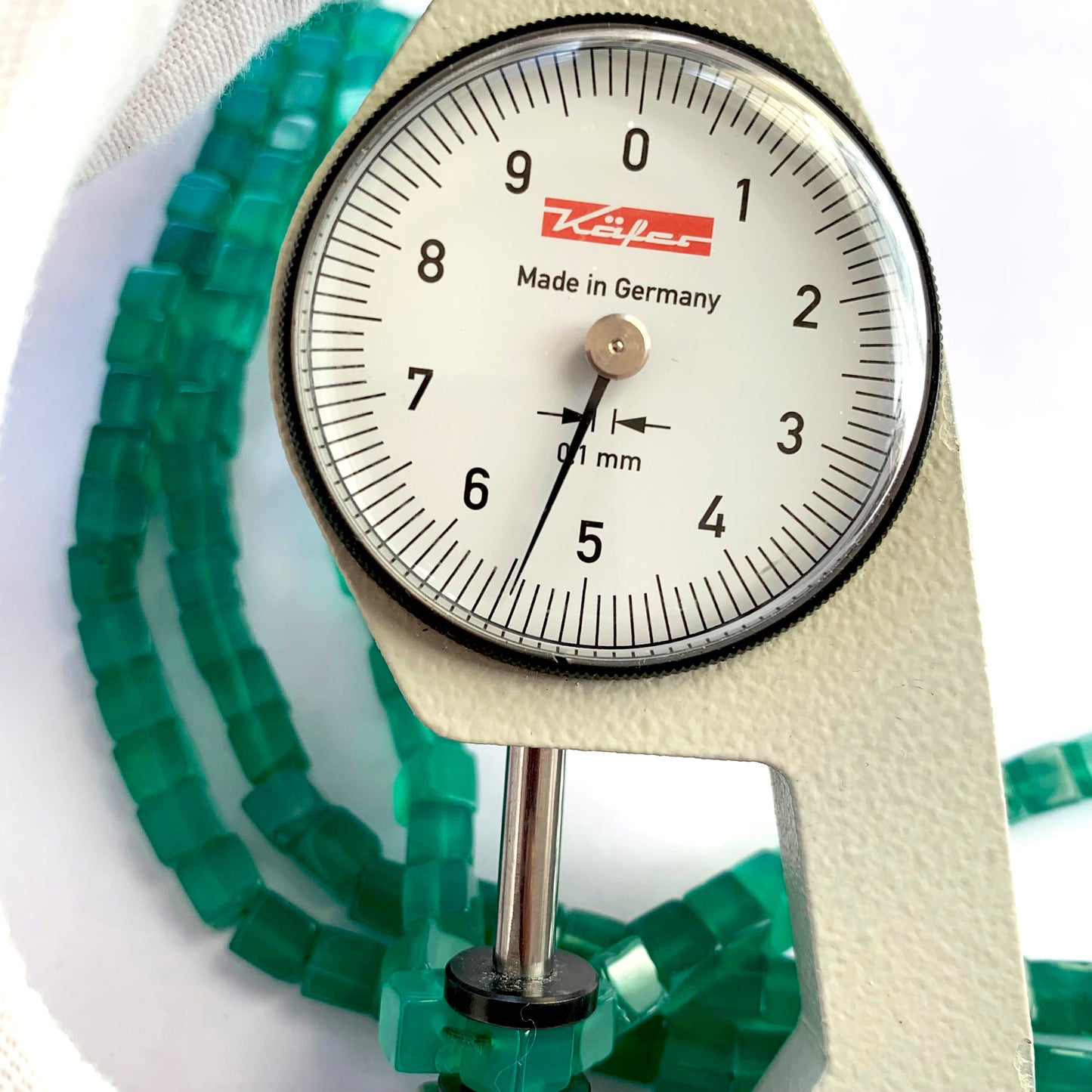 A dial gauge measures the Onyx Smooth Cube 5.5mm gemstone, confirming precision cutting.