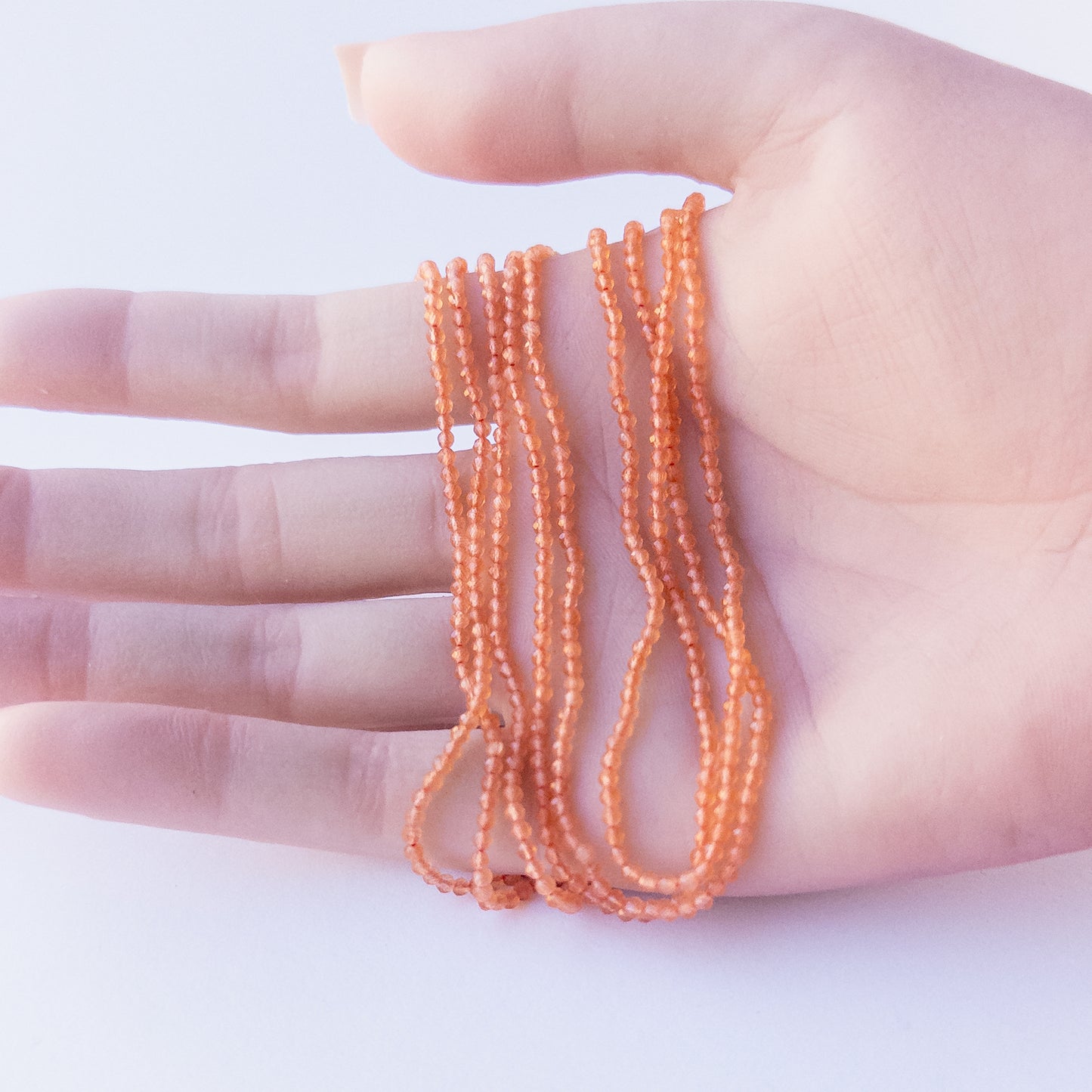A person holds delicate strands of Orange Chalcedony beads, showcasing their faceted rondelle design.