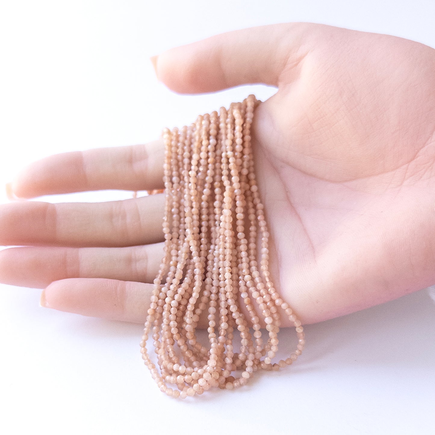 A person holds delicate strands of Peach Moonstone beads, showcasing their faceted rondelle design.