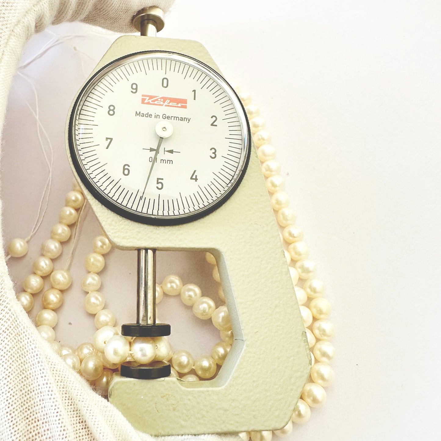 A dial gauge measures the pearl round 5.4-5.6mm gemstone.