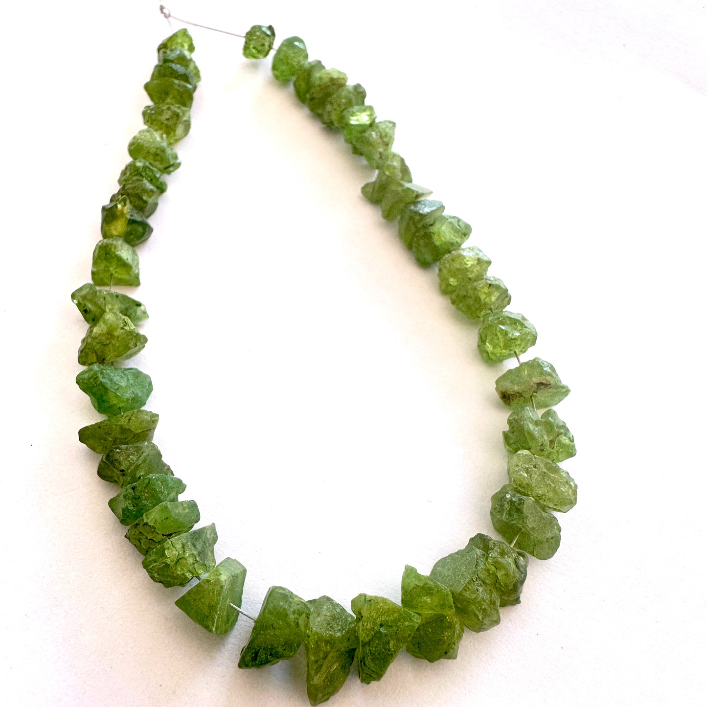 Faceted light catching on rough peridot beads with earthy green hues and matte finish.