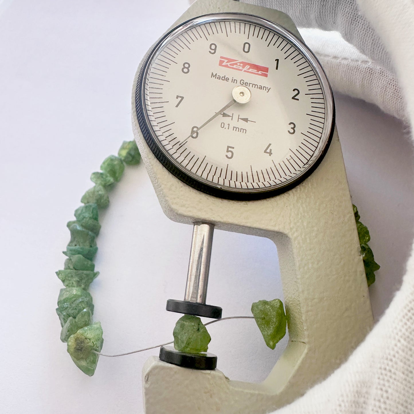 A dial gauge measures the peridot rough centre drilled 7.5-9mm gemstone.