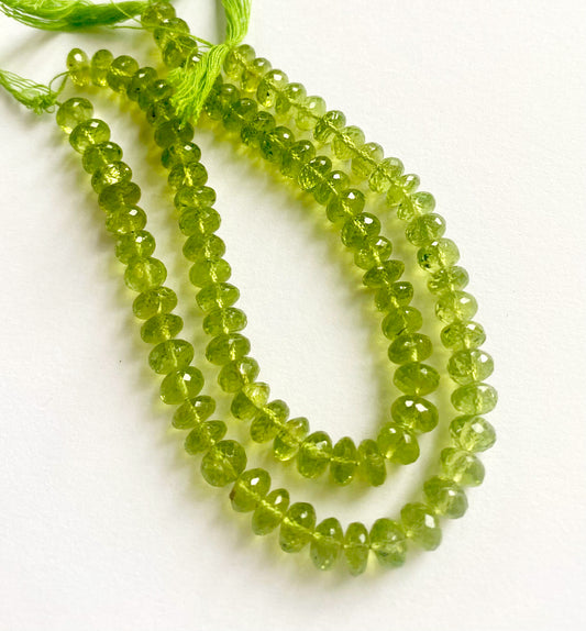 Glossy Peridot beads in rondelle shape, stacked uniformly against a contrasting background.