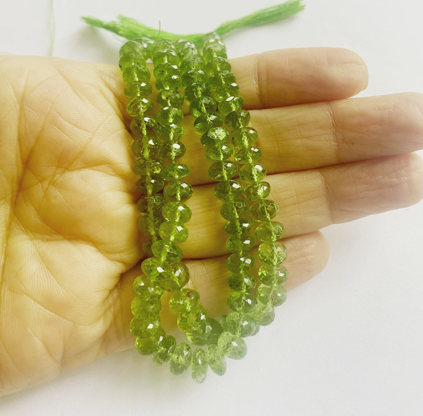 A person holds delicate strands of Peridot beads, showcasing their smooth design.