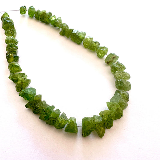 Close-up of raw peridot gemstones arranged in a 43-piece strand with organic texture.