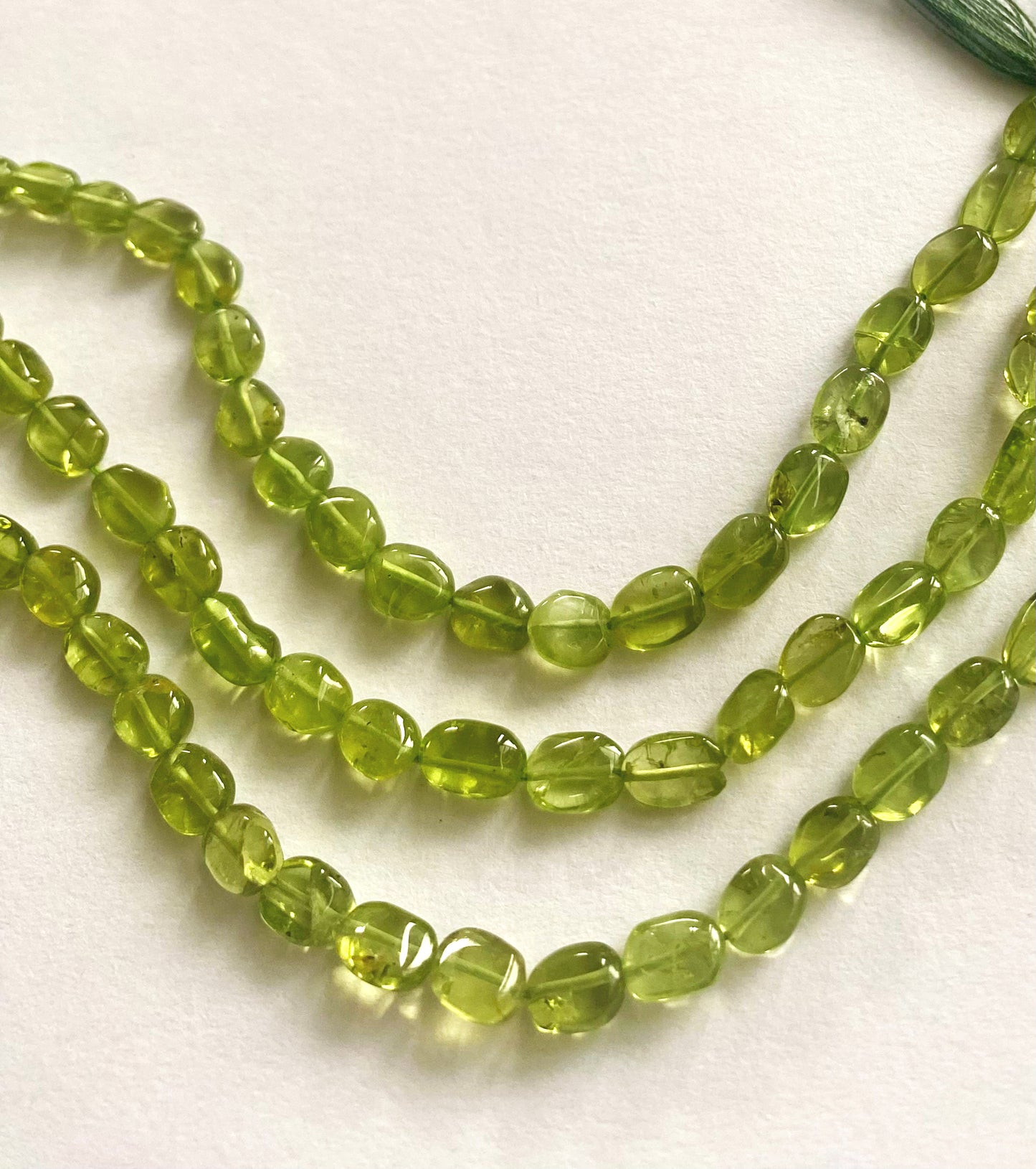 Strand of peridot beads with 6.5–7.5mm size, highlighting their smooth finish and bright colour.