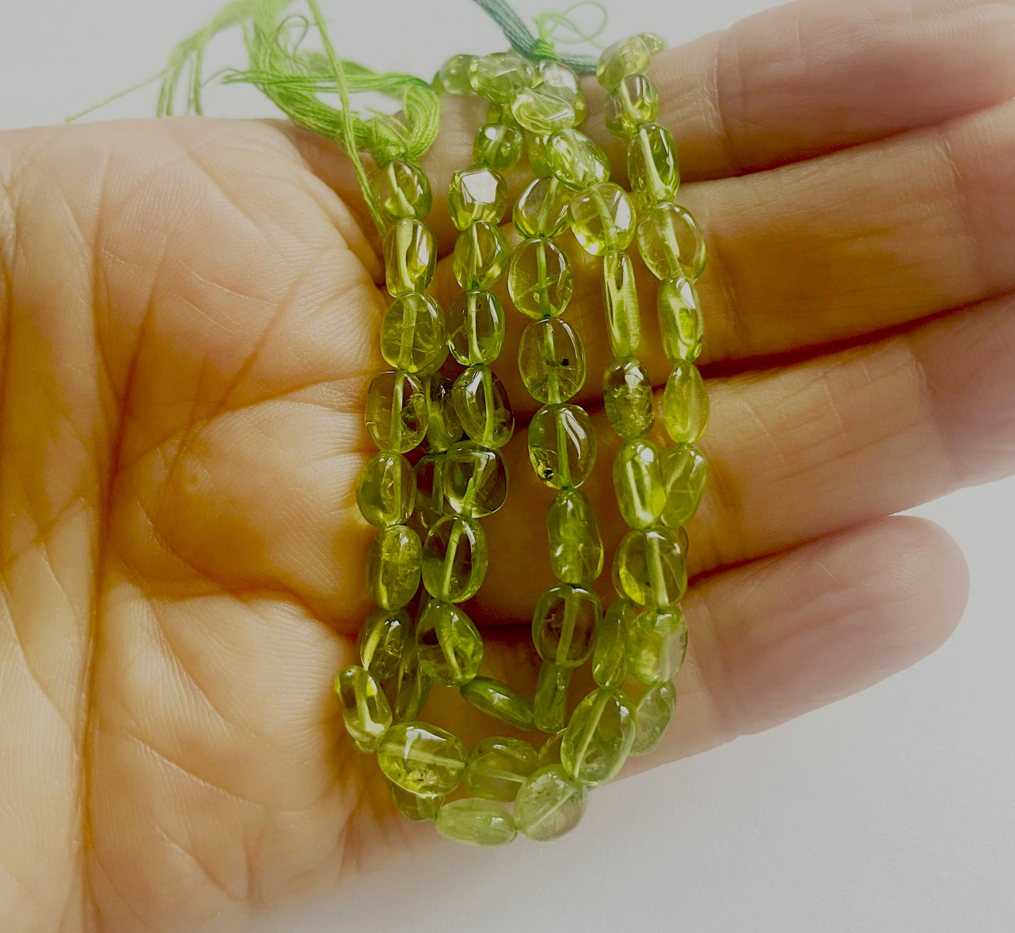 A person holds delicate strands of peridot beads, showcasing their smooth design.