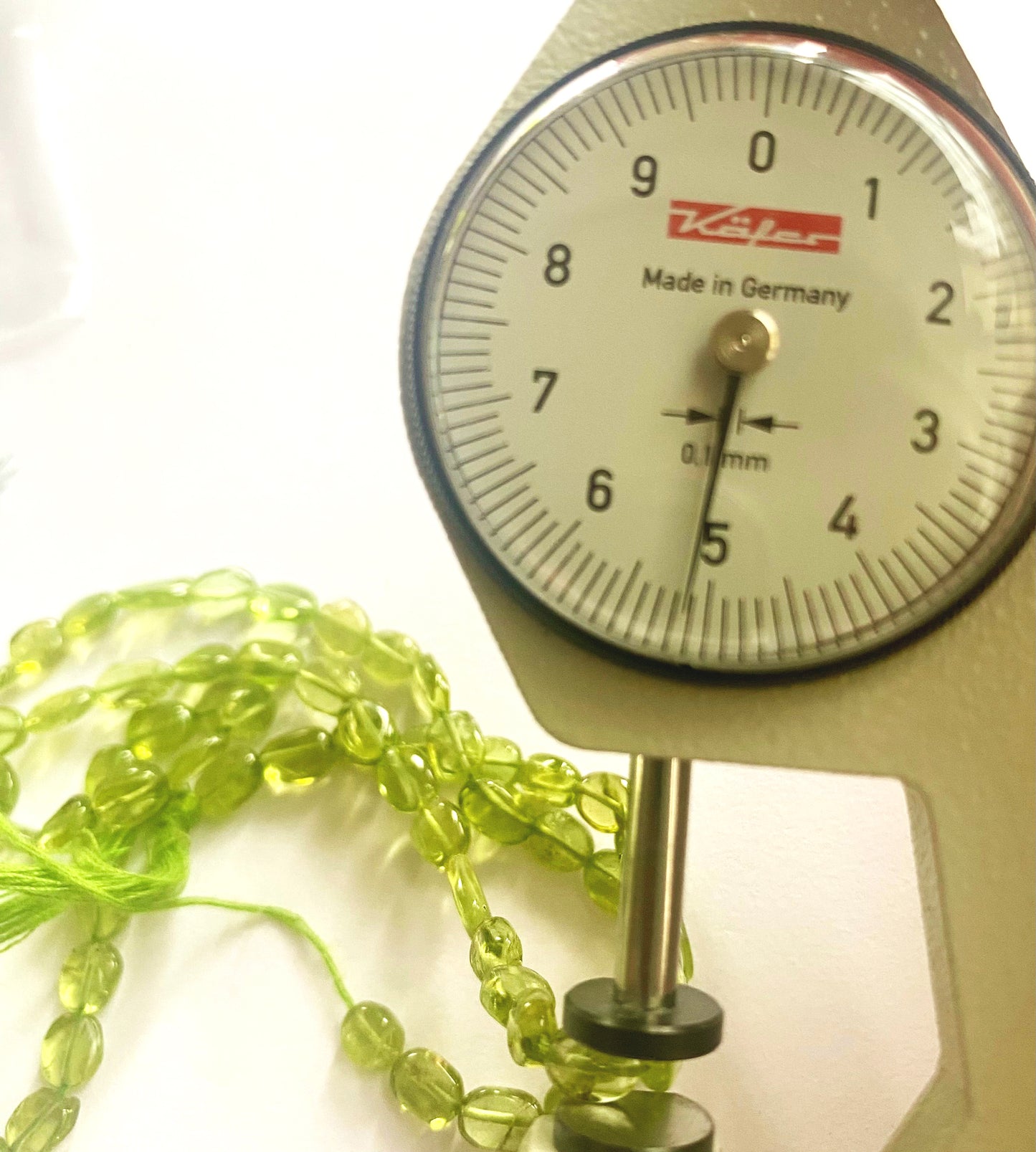 A dial gauge measures the peridot smooth oval 6.5–7.5mm gemstone.