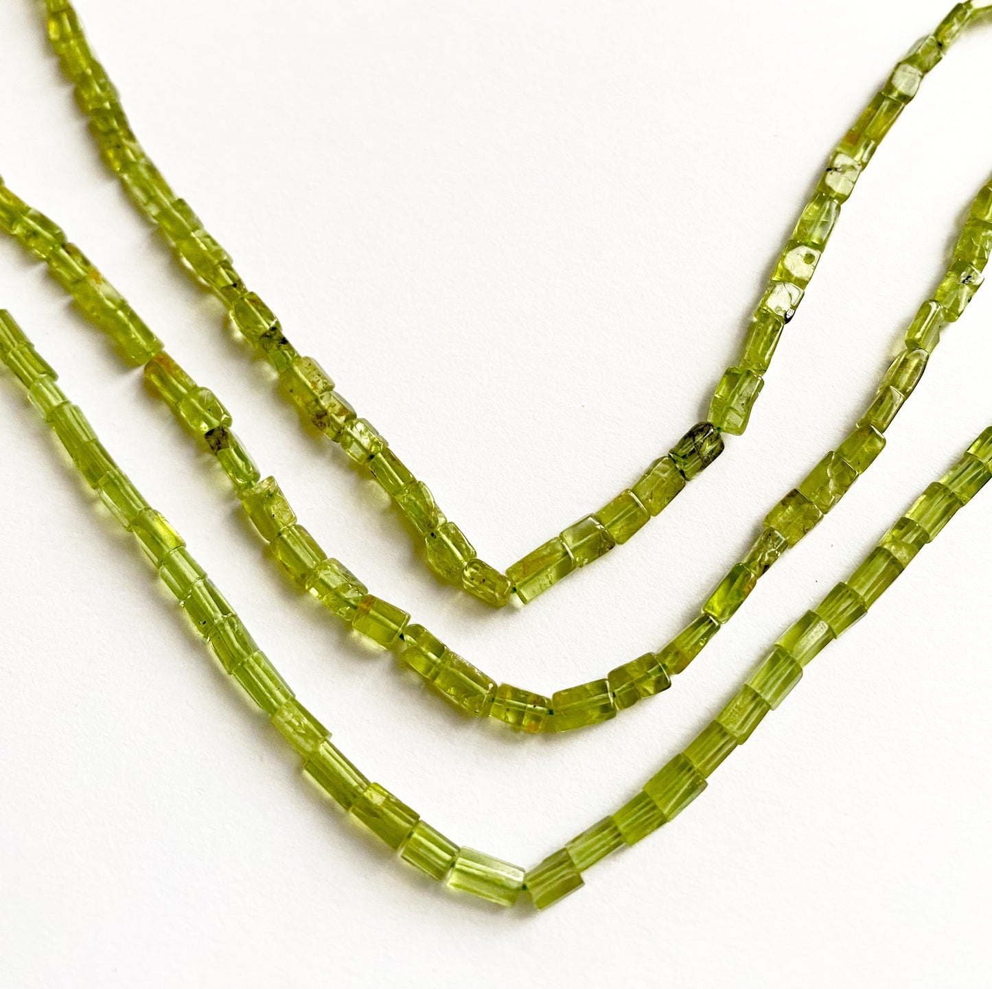 Macro shot capturing the translucent green glow of Peridot tube cut beads, 4.5–6mm in length.