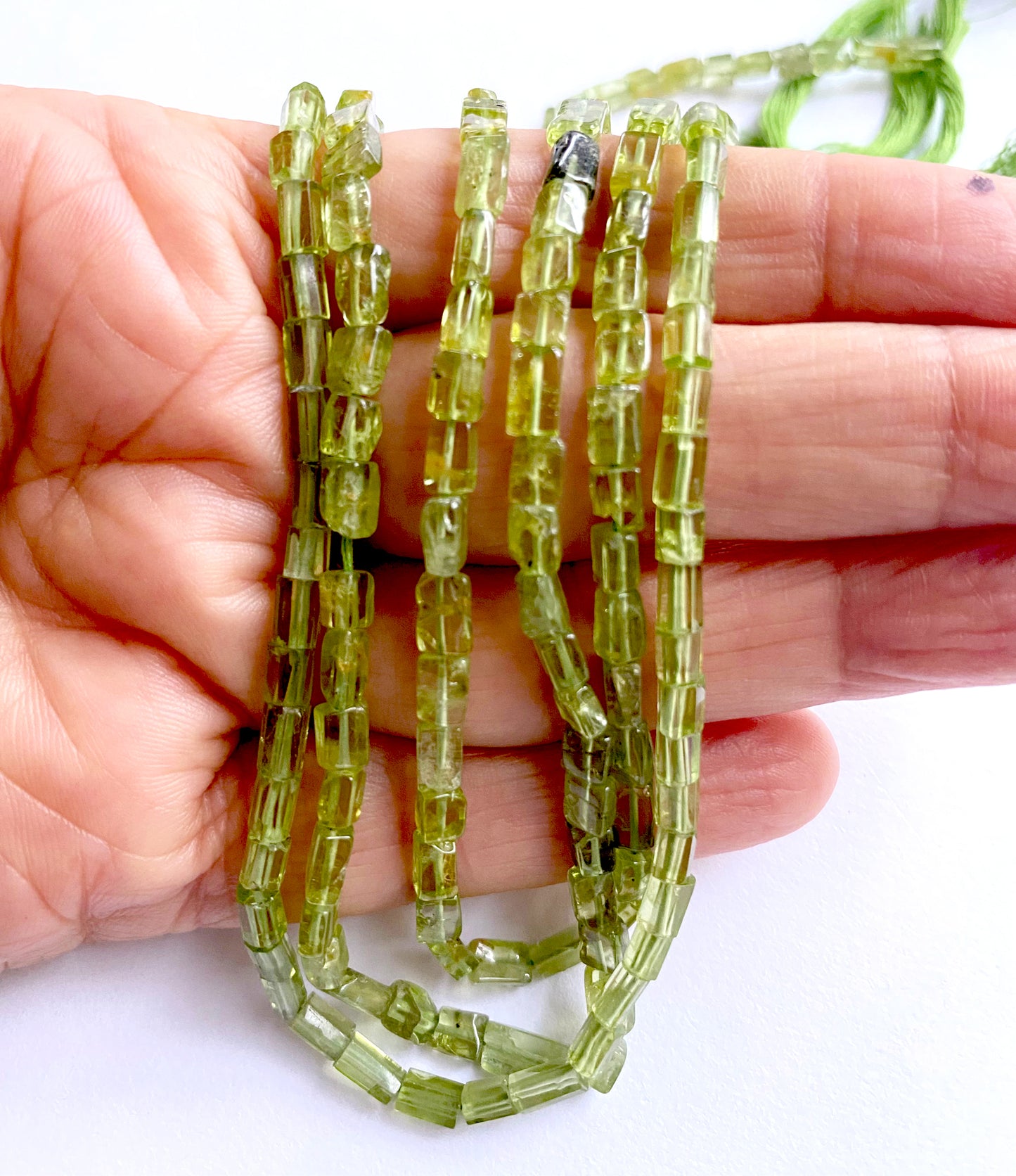A person holds delicate strands of Peridot beads, showcasing their smooth design.