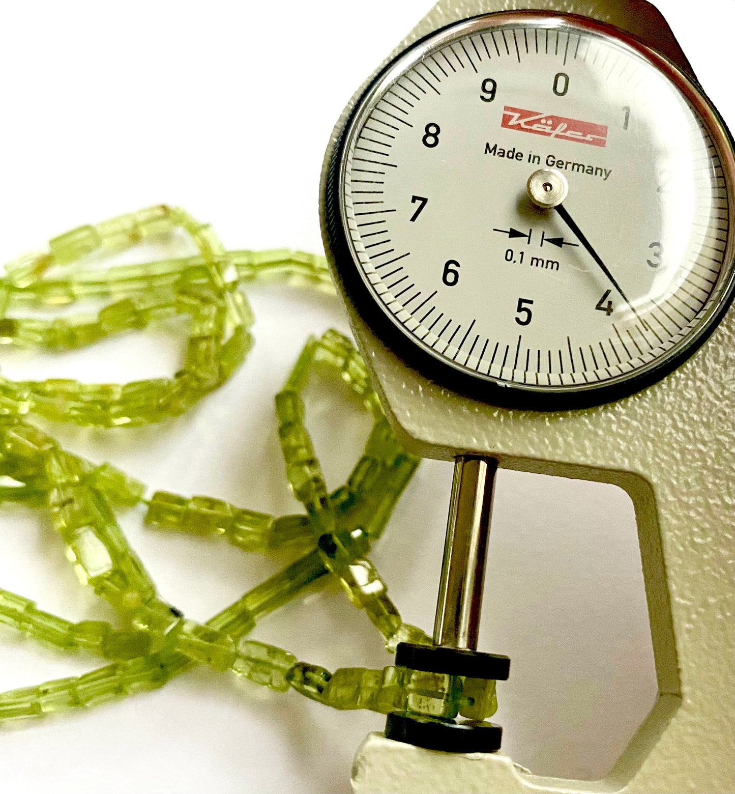 A dial gauge measures the Peridot tube beads, demonstrating accurate sizing of 4.5–6mm length and 3.5–4.0mm width.