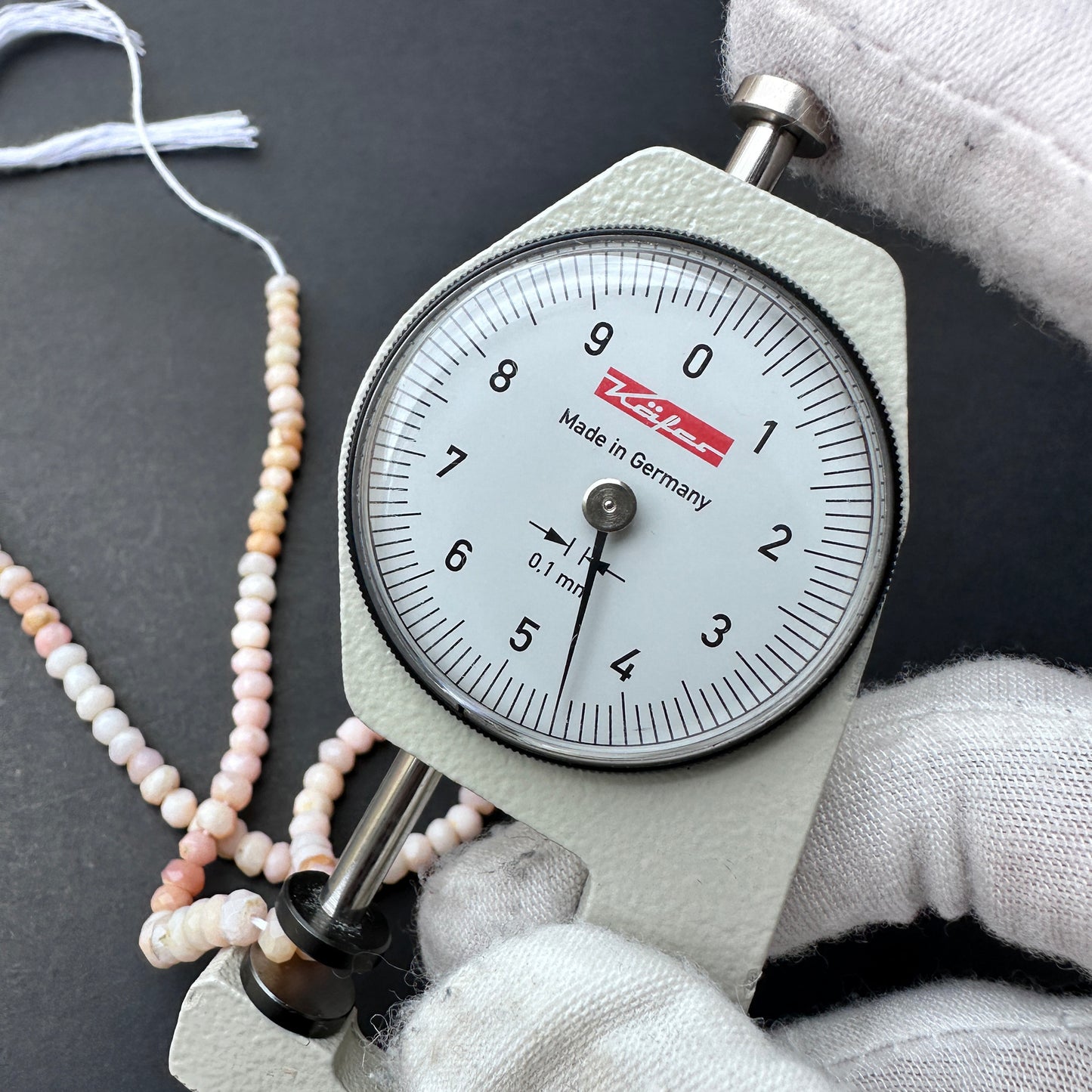 A dial gauge measures the Pink Shaded Opal faceted rondelle 4.2-4.5mm gemstone.