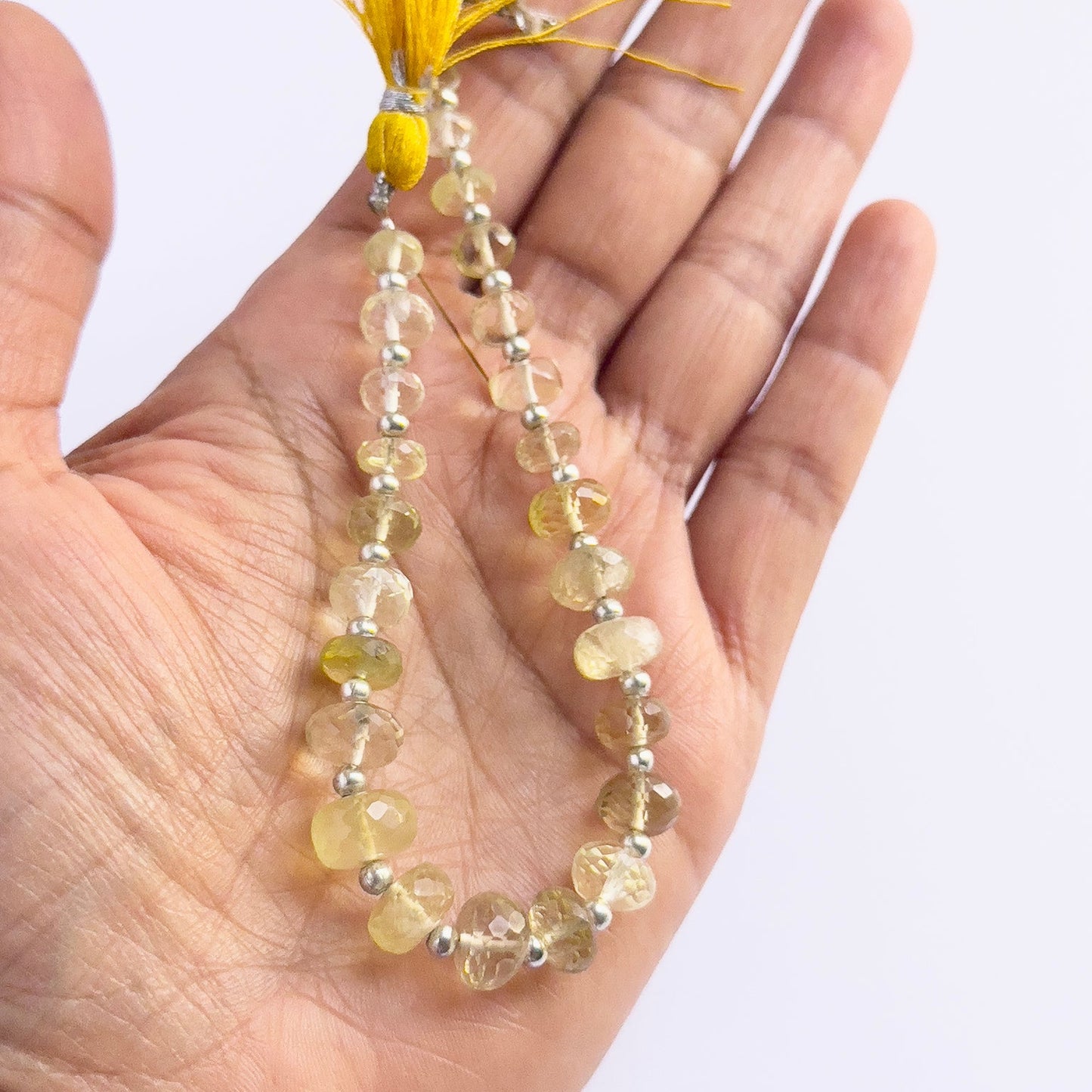 A person holds delicate strands of Prehnite beads, showcasing their smooth design.